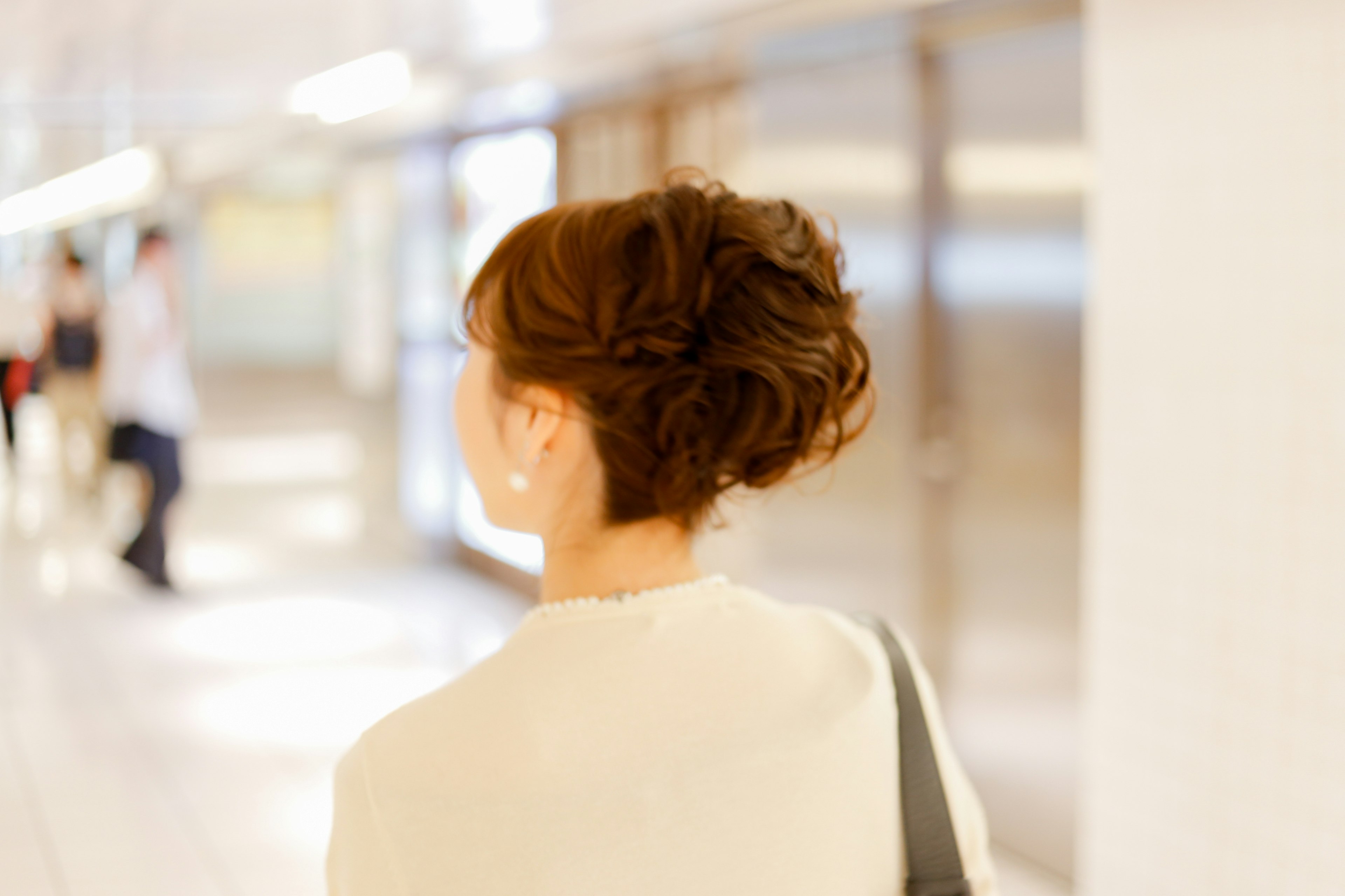 Une femme vue de dos marchant dans un couloir de gare avec une coiffure distinctive