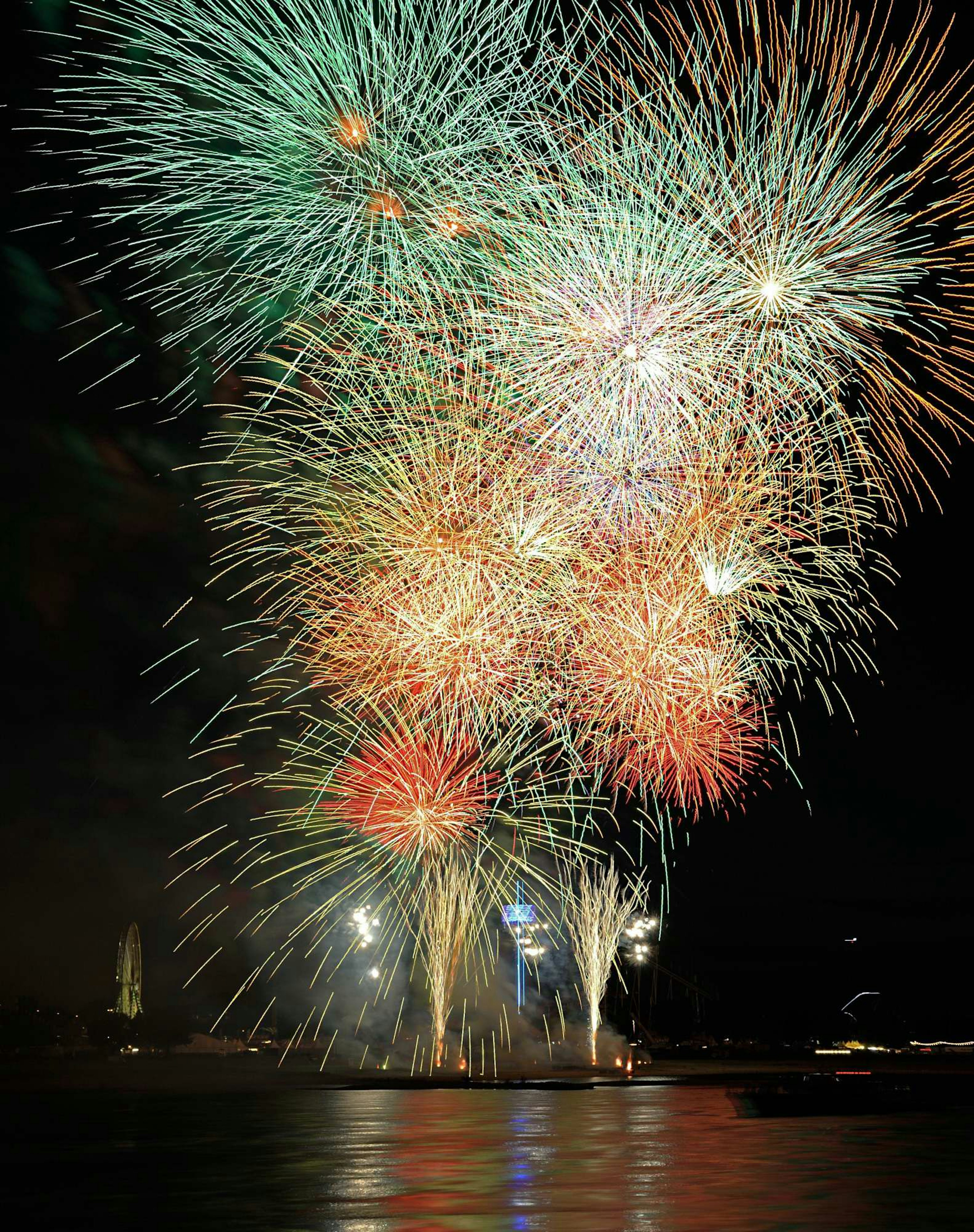 Spectacle de feux d'artifice vibrant illuminant le ciel nocturne avec des éclats colorés se reflétant sur l'eau