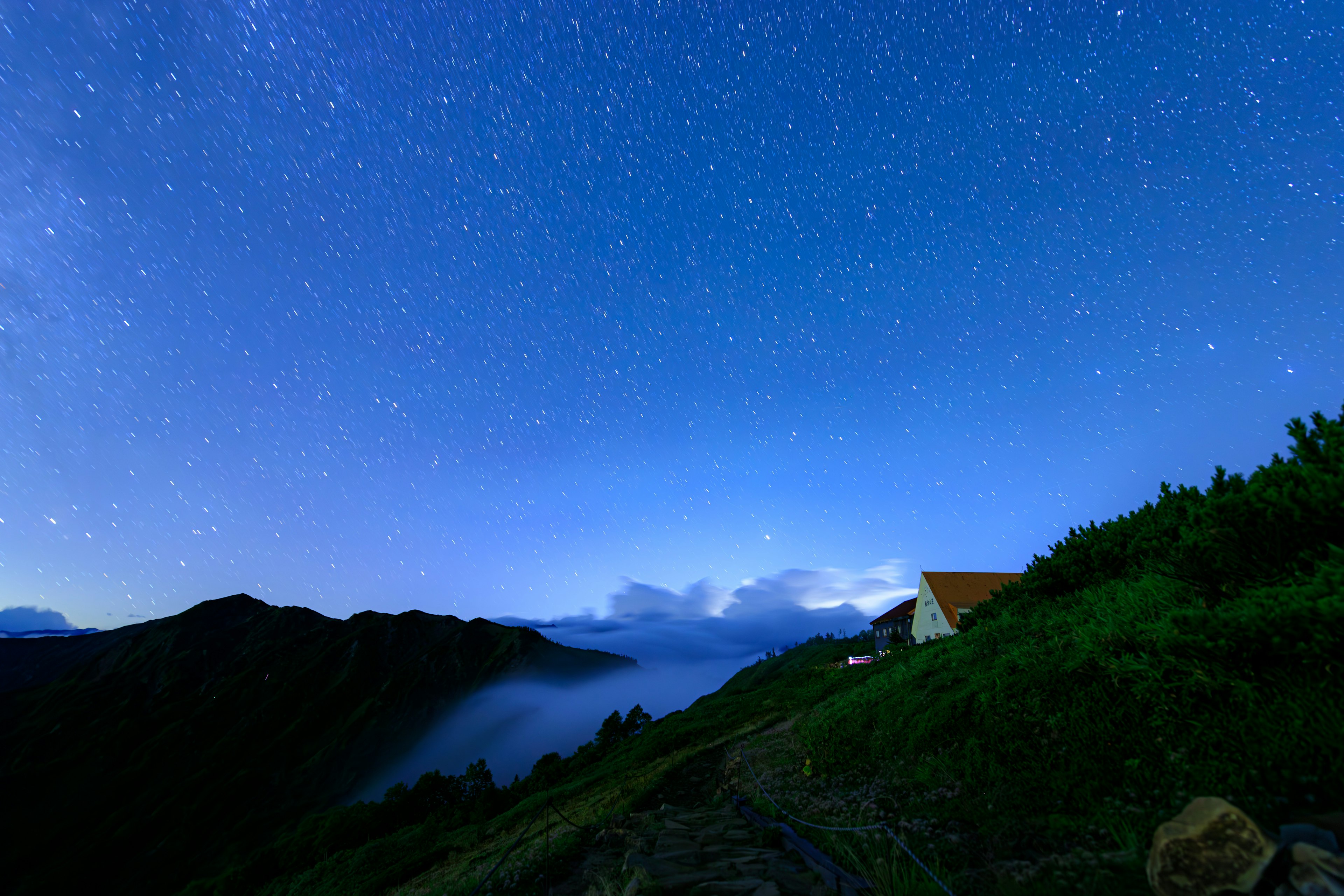 Un paysage nocturne avec un ciel étoilé et des nuages, des montagnes et une maison