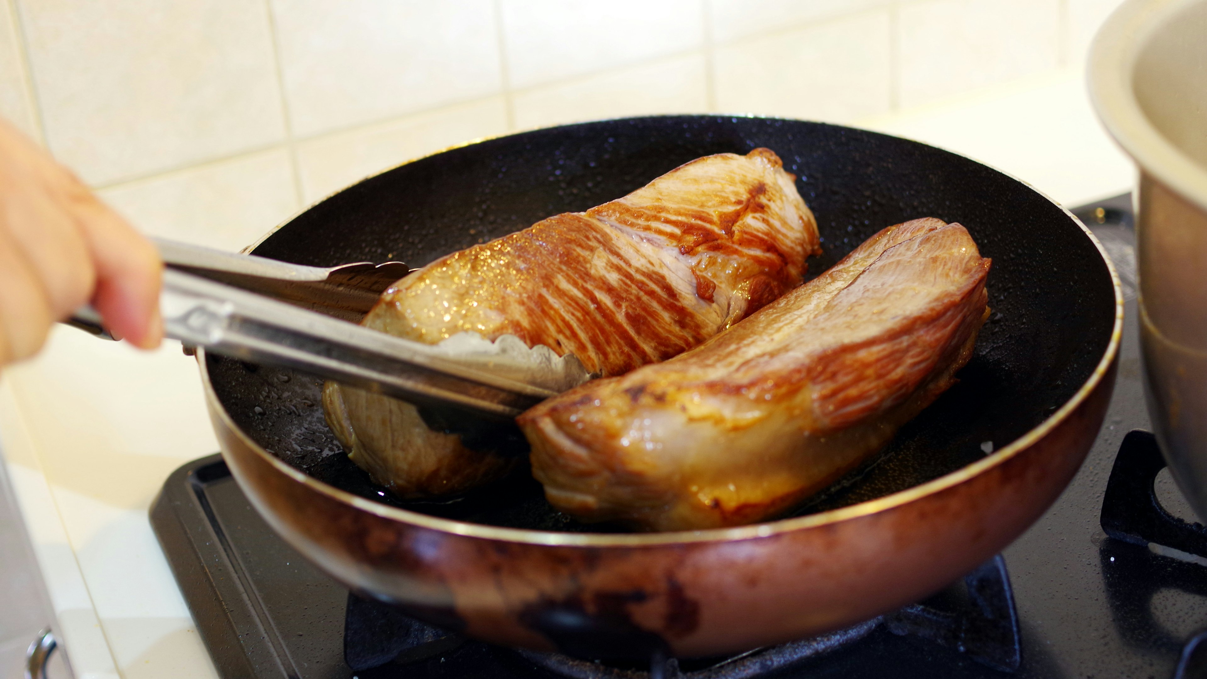 Hand, die Fleisch in einer Pfanne wendet