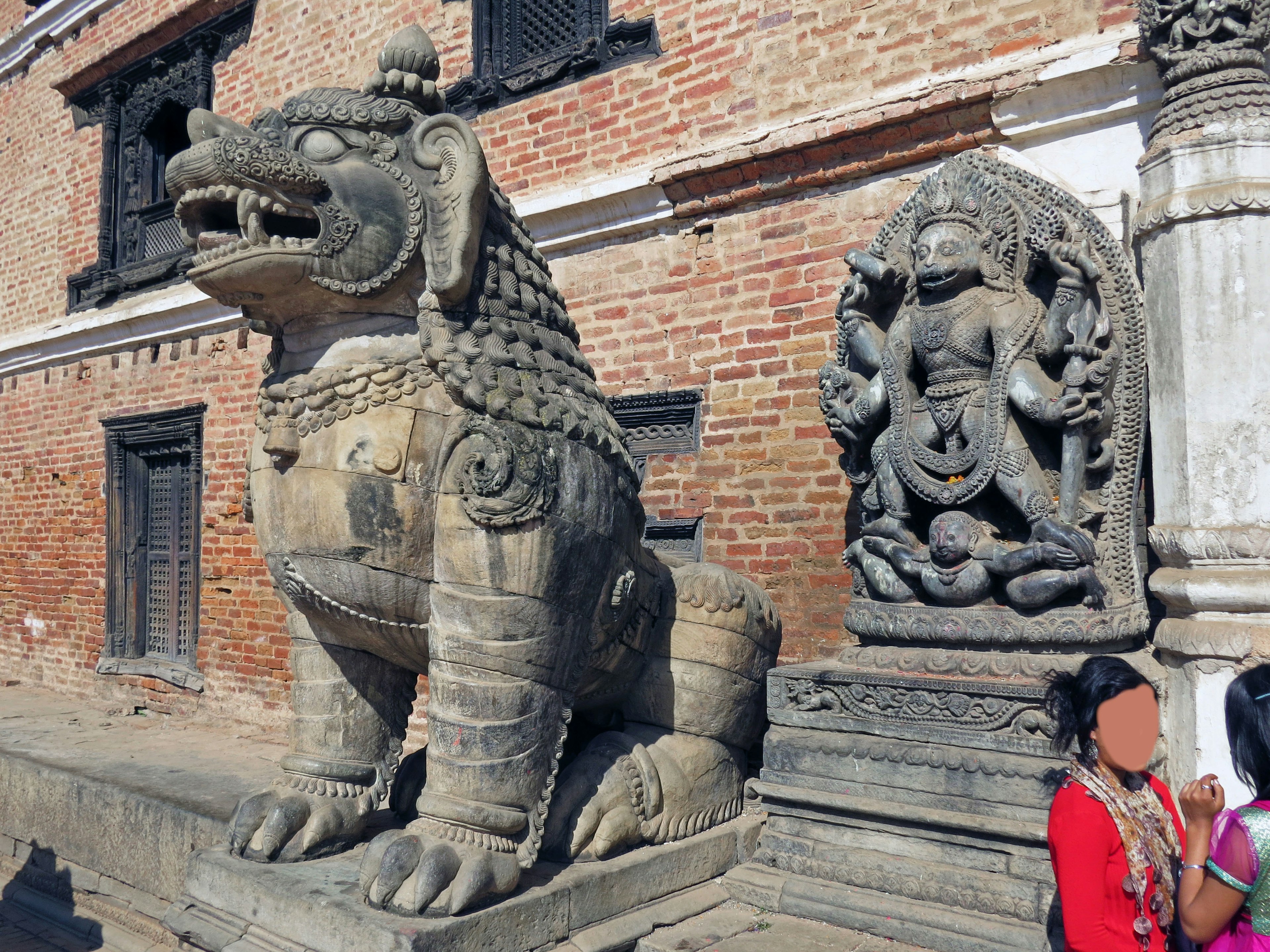 Estatua de león de piedra y escultura de deidad junto a un edificio antiguo