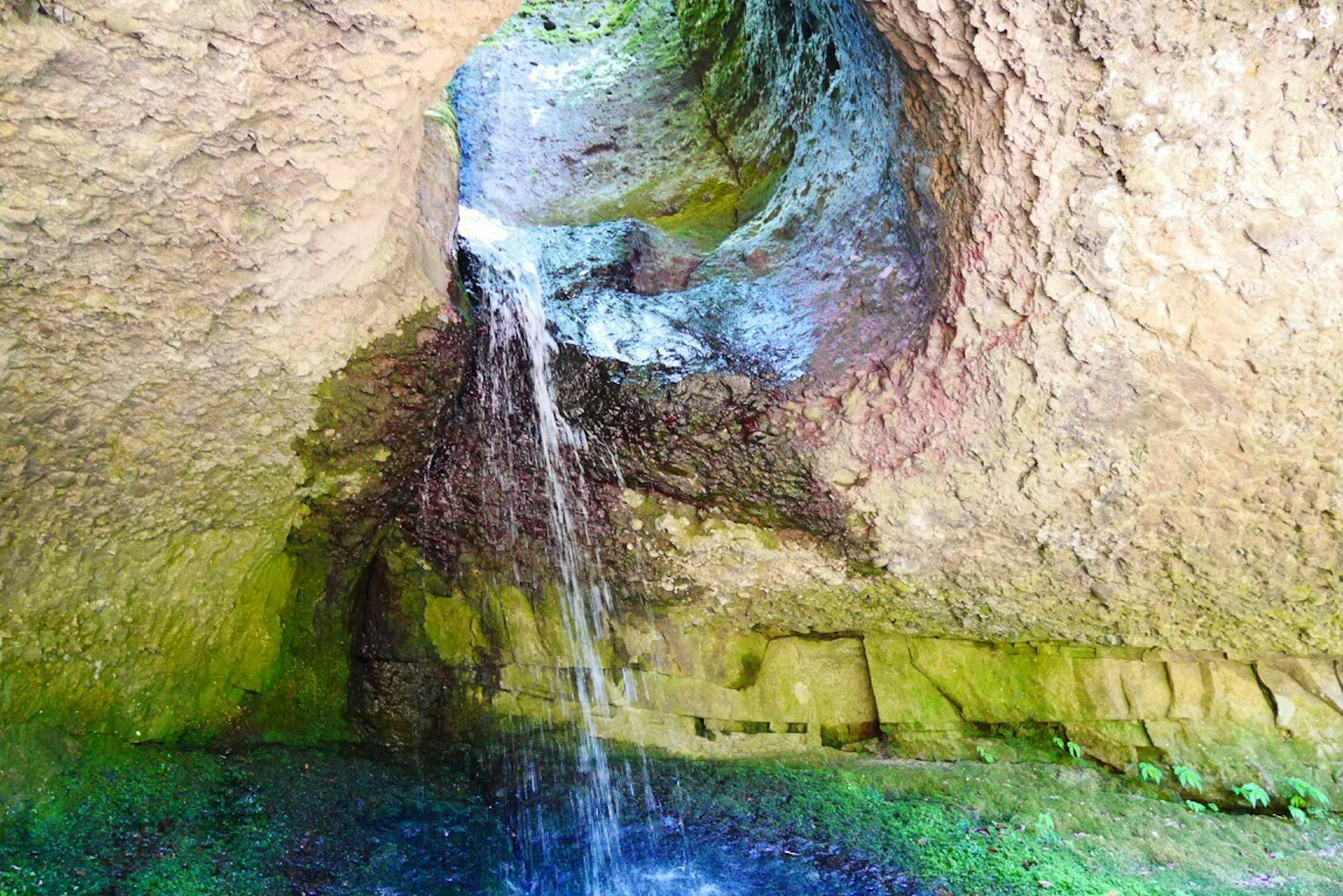 Pemandangan alami dengan air mengalir dari gua dan kolam hijau