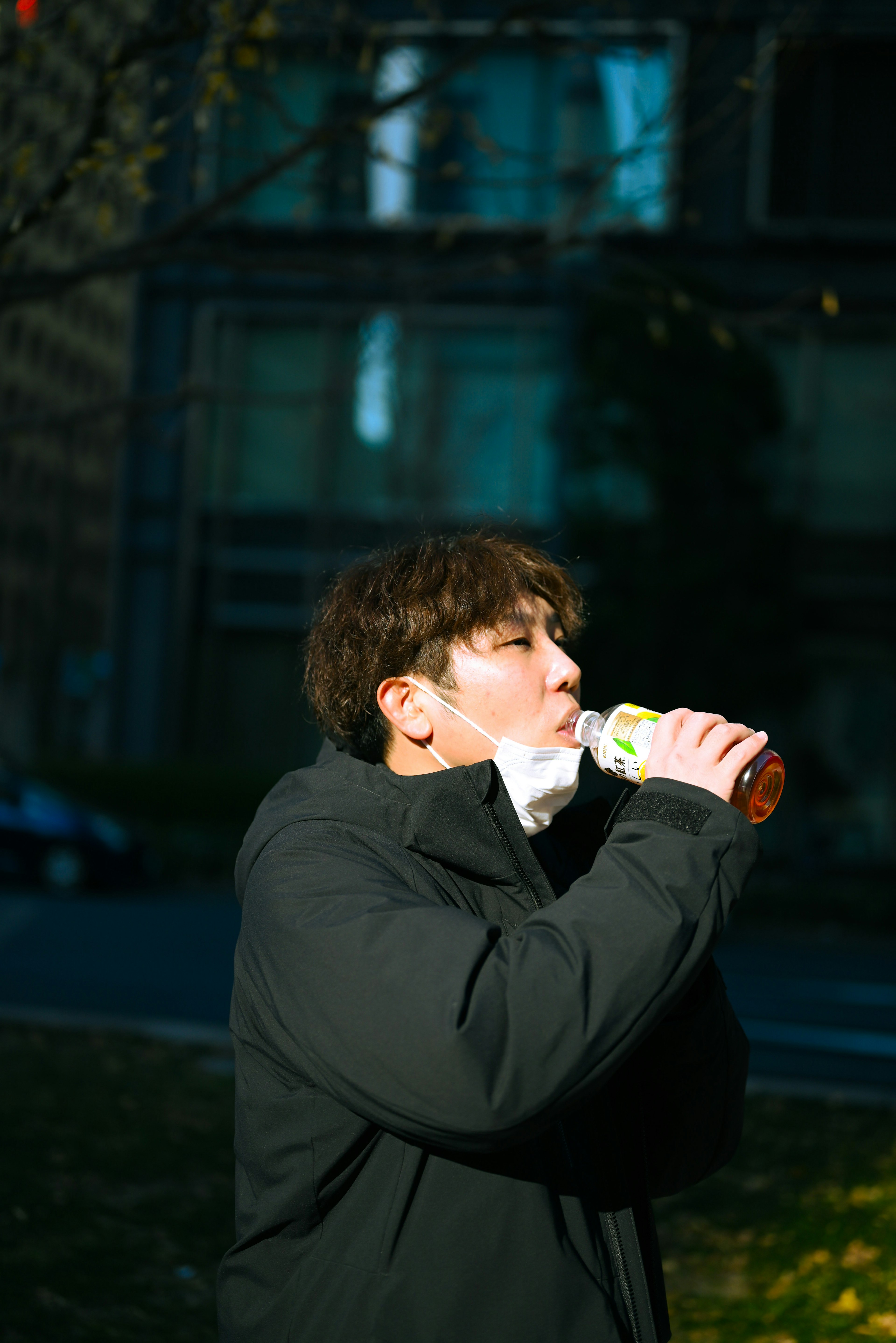 Man in black jacket drinking from a bottle outdoors