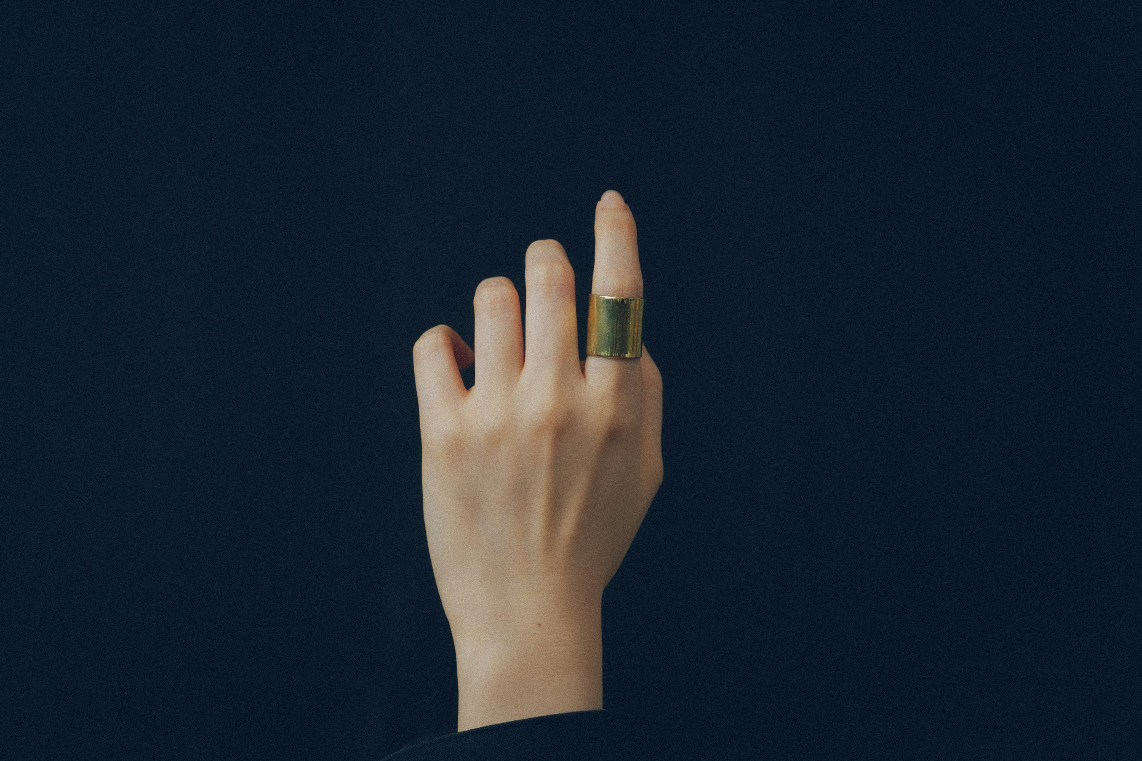 Une main avec une bague verte pointant vers le haut sur un fond sombre