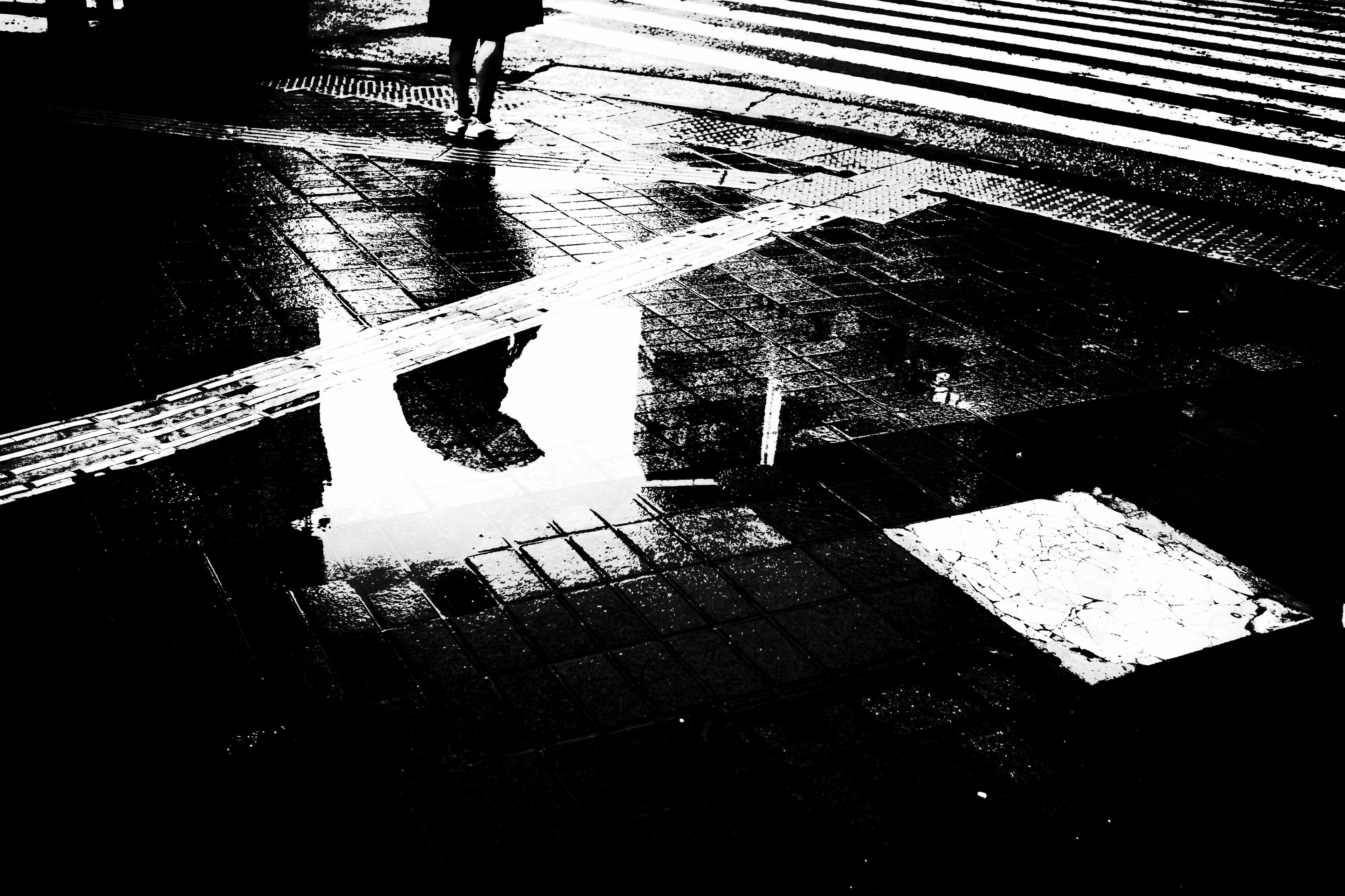 Trottoir mouillé reflétant un passage piéton après la pluie