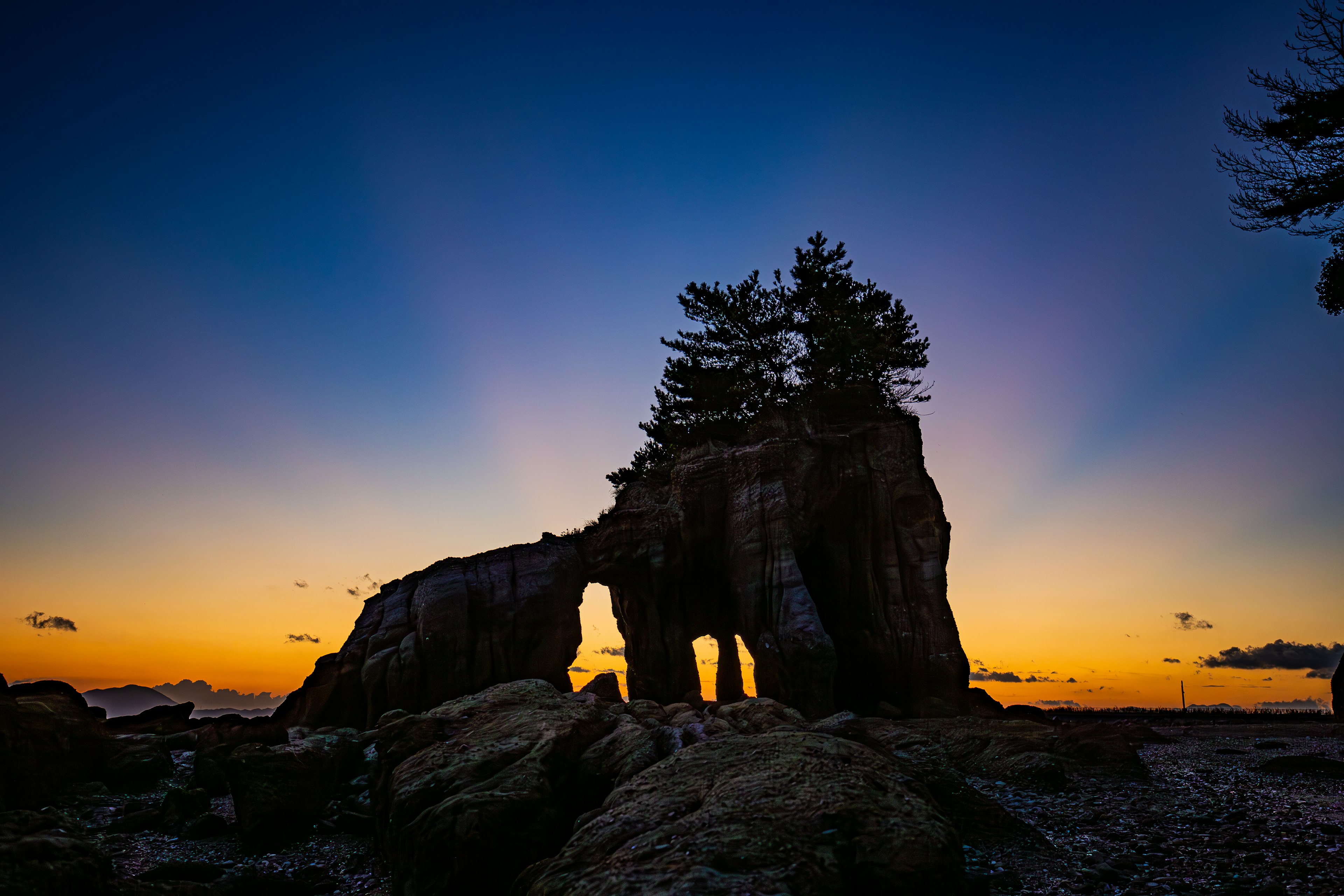 Silhouette eines Felsenbogens und Bäume vor einem bunten Sonnenuntergang