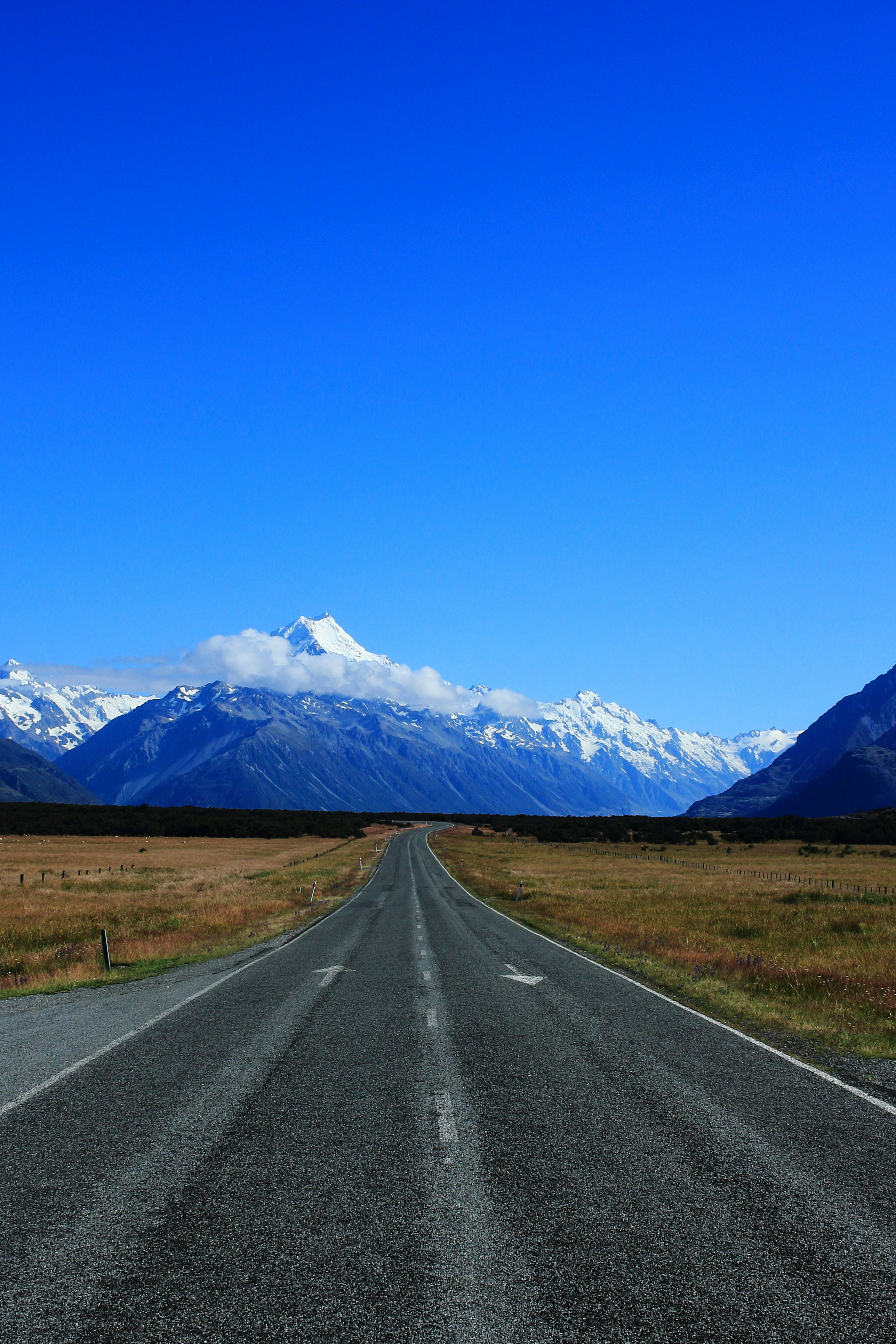 A road stretching towards snow-capped mountains under a clear blue sky