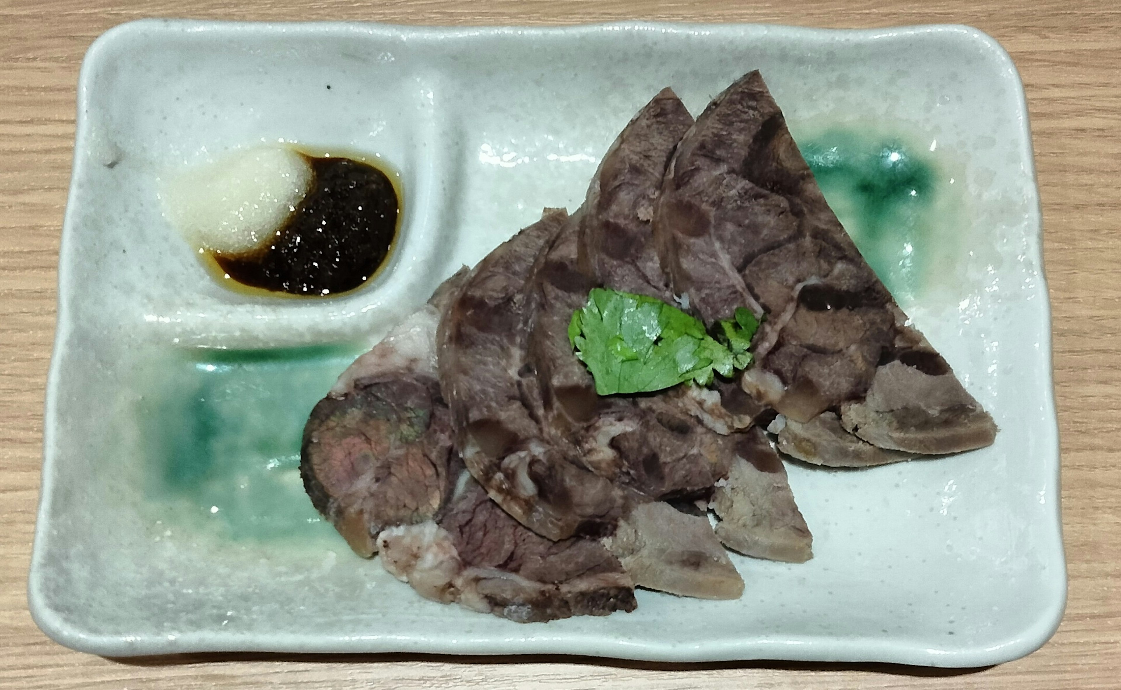 Carne en rodajas servida en un plato con salsa para mojar