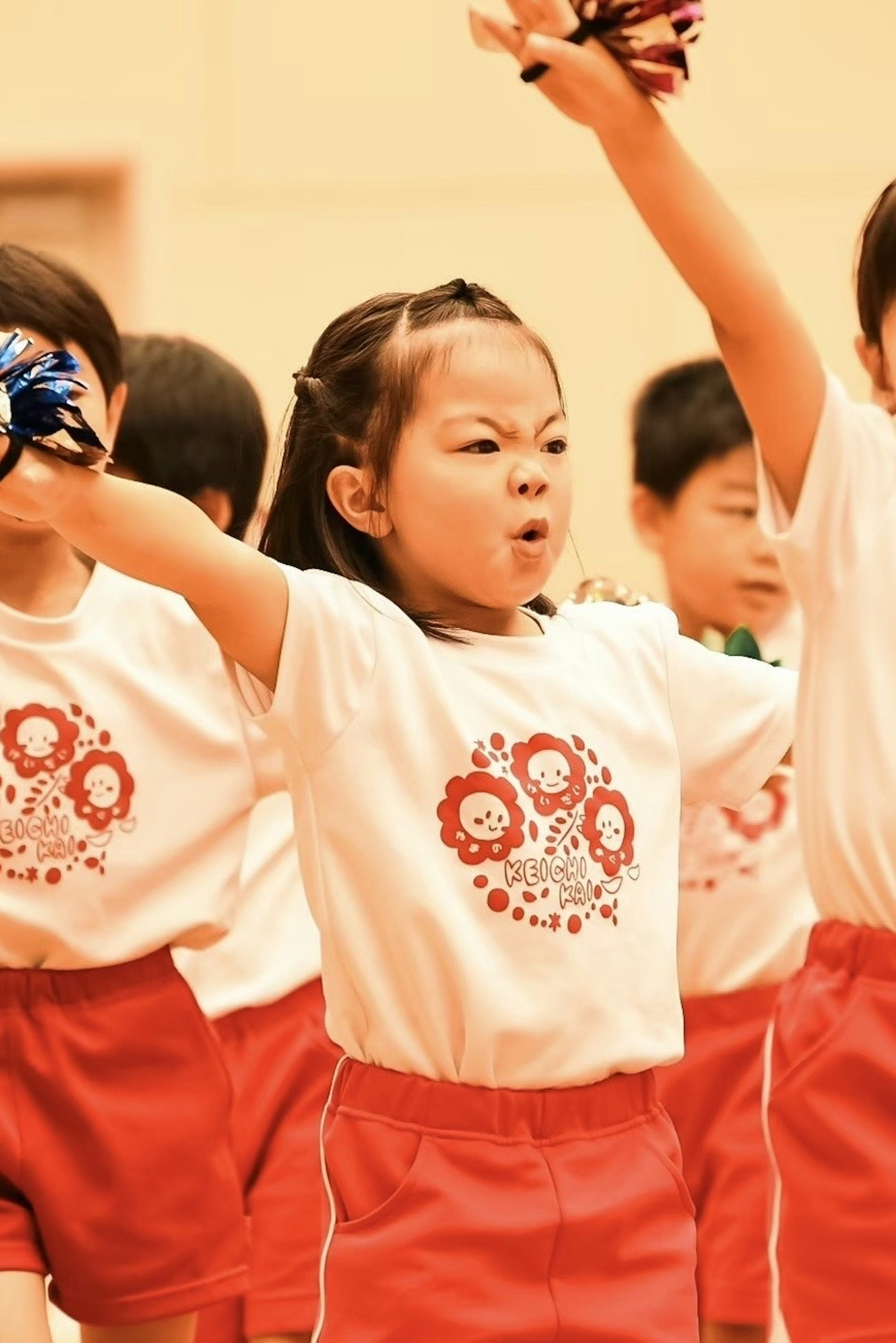 元気にパフォーマンスする子供たちのグループ　赤いショートパンツと白いTシャツを着た女の子　ポンポンを持っている　集中した表情