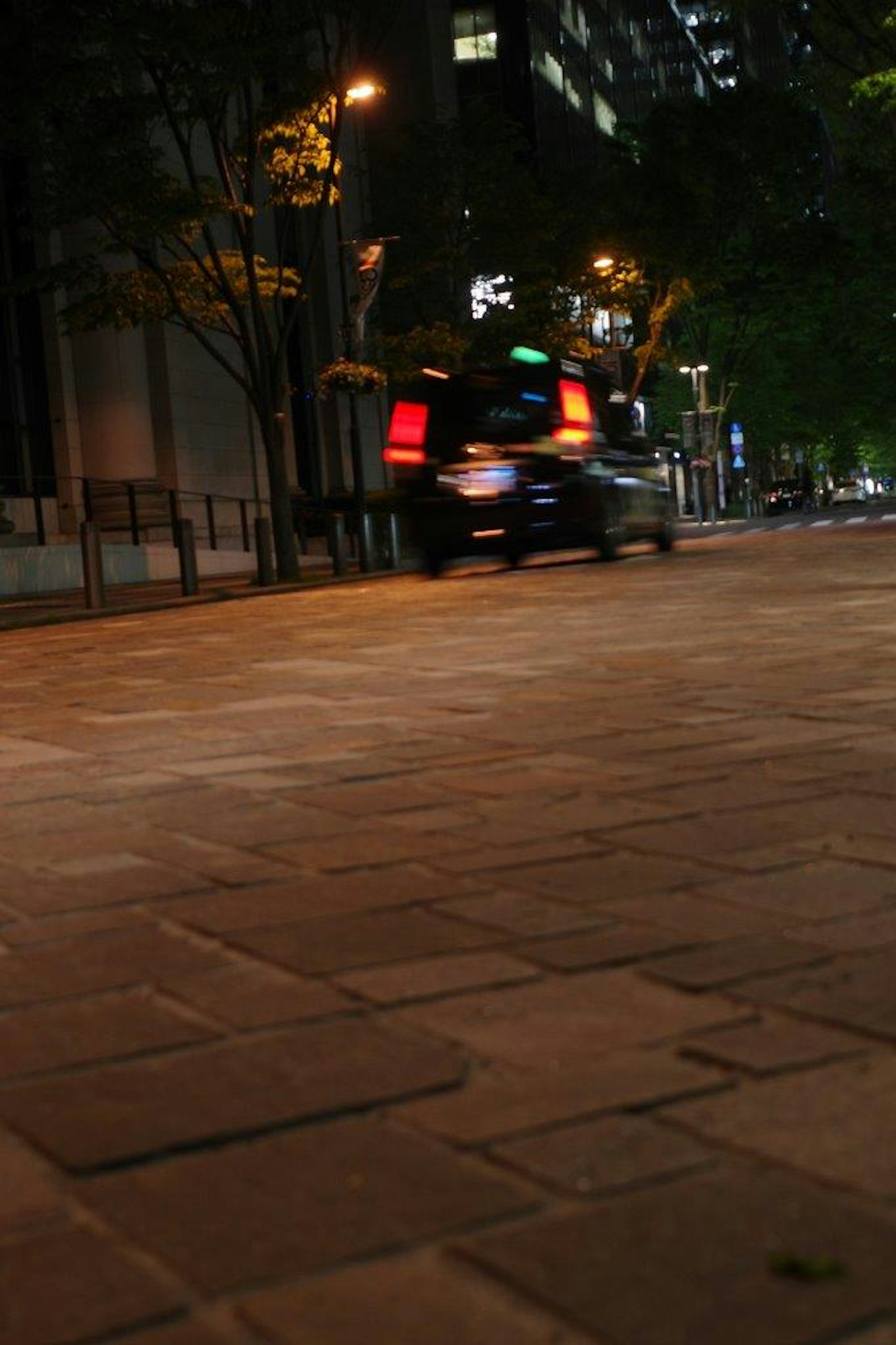 夜の街並みで走る車の後ろ姿と石畳の道路