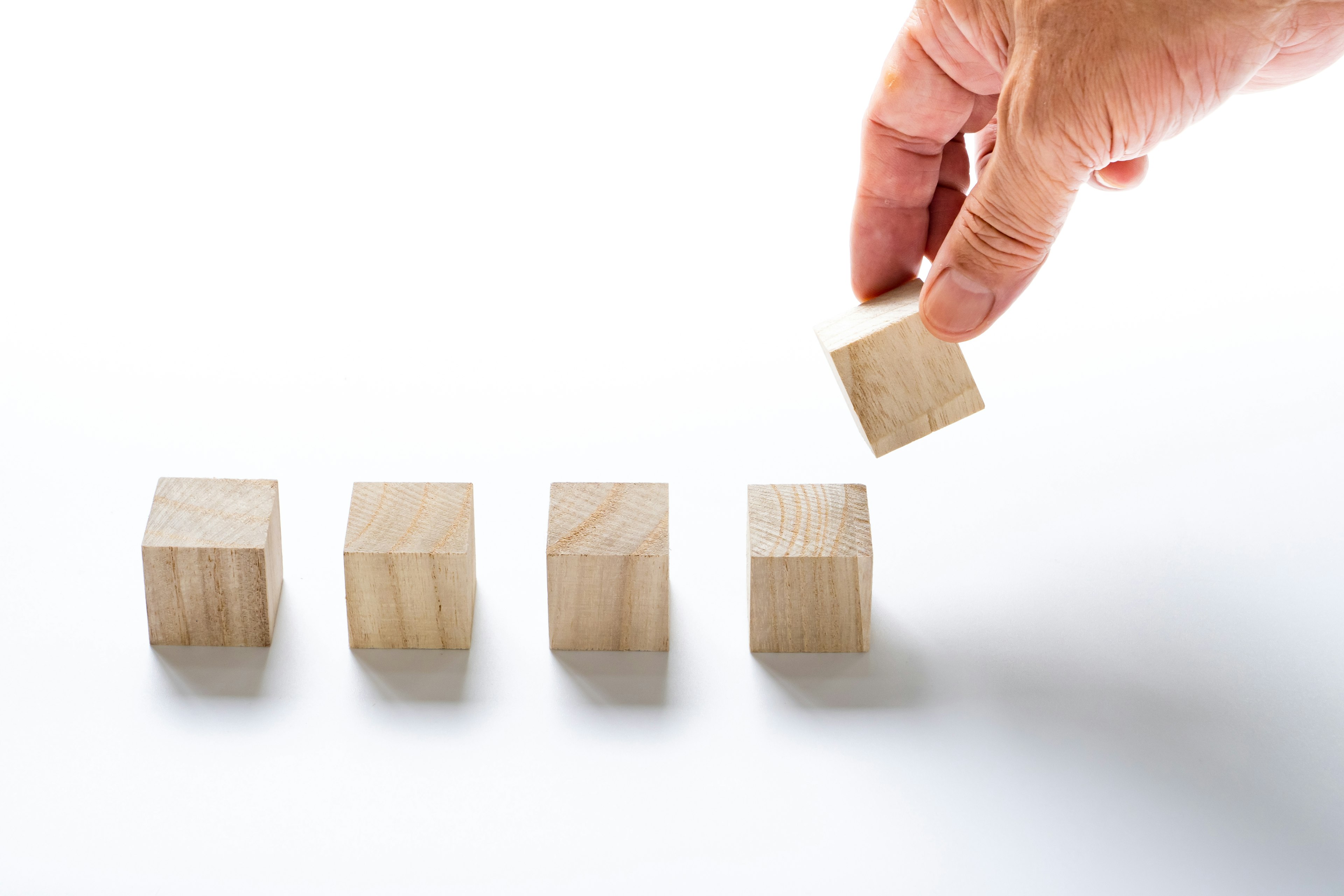 A hand picking up a wooden block with four blocks arranged on a white background