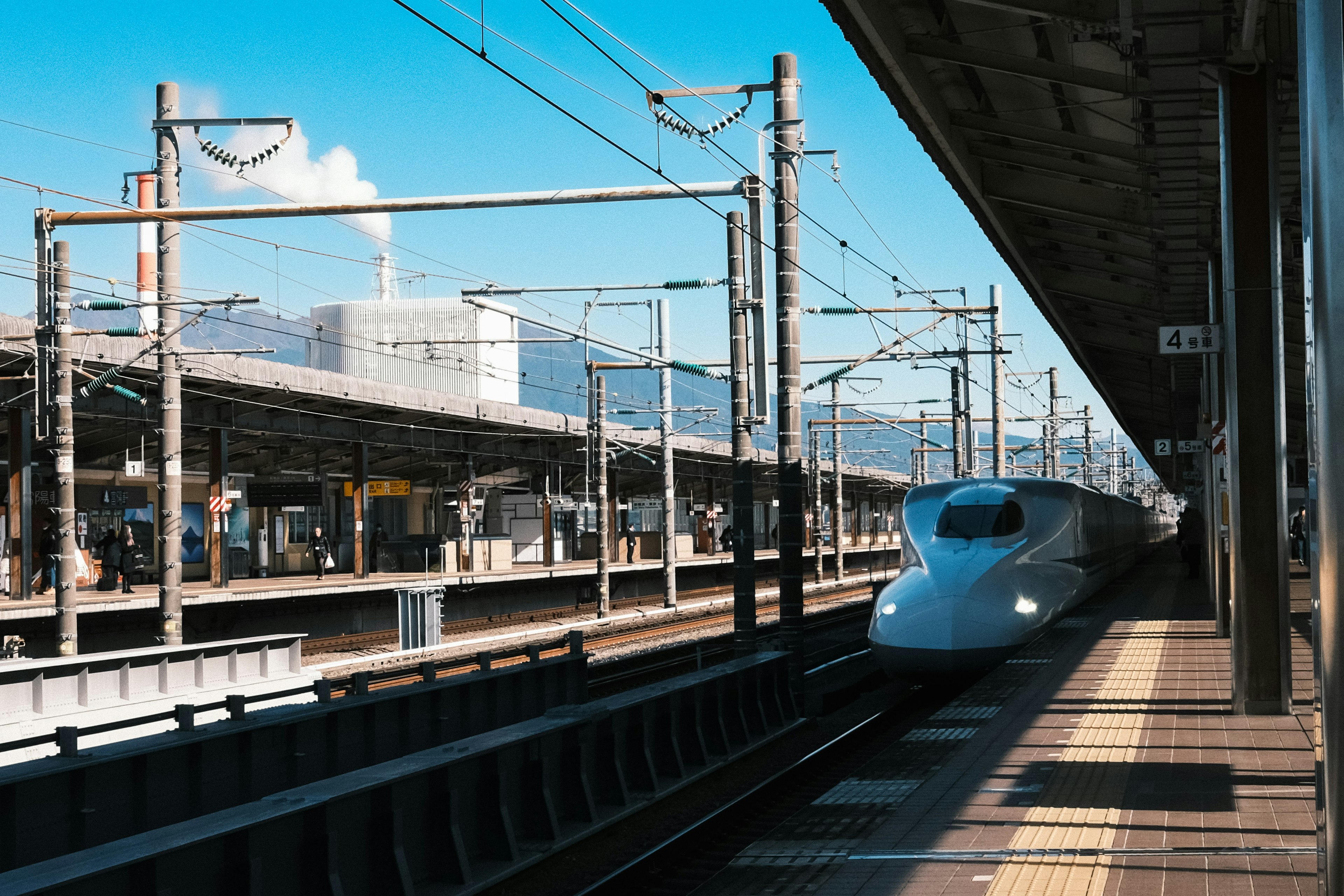 Kereta Shinkansen tiba di stasiun dengan latar belakang langit biru dan gunung