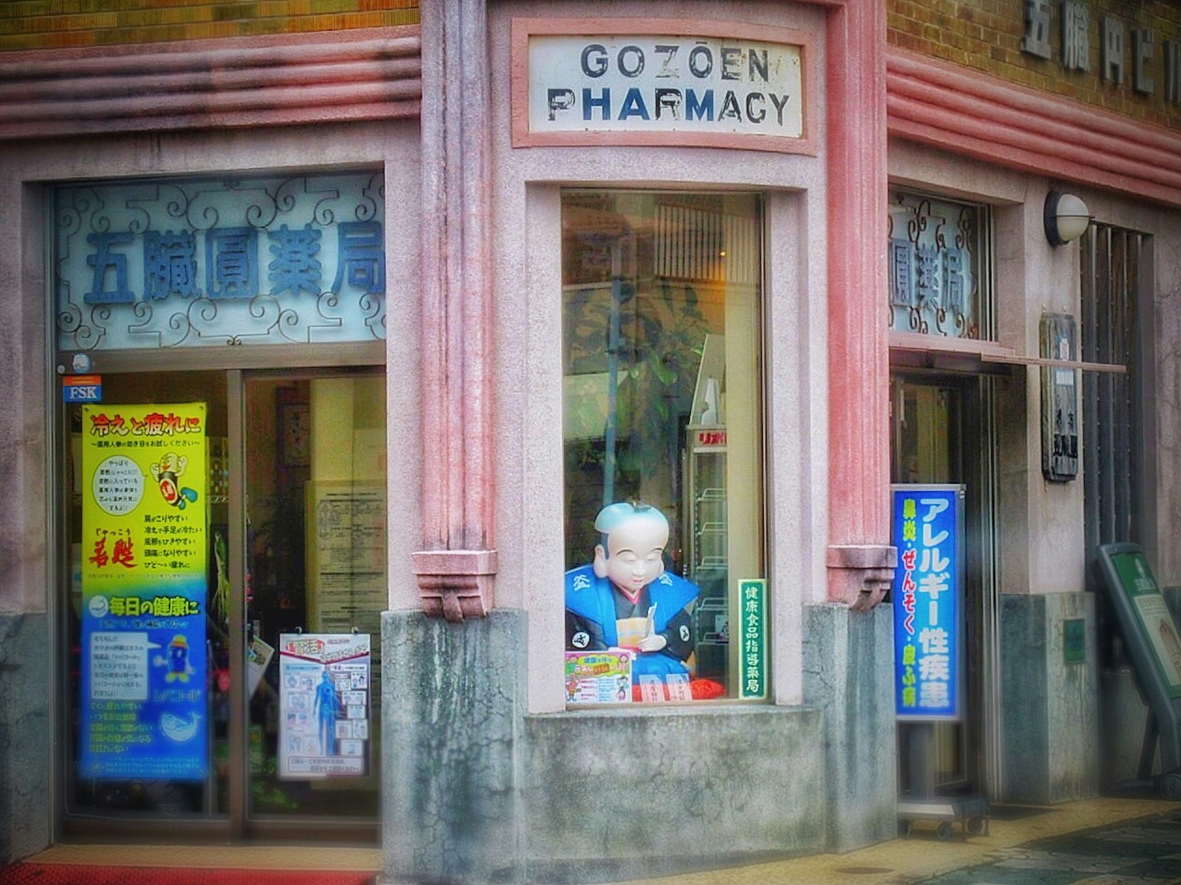 Una fachada de farmacia rosa con una figura de cabello blanco en la ventana