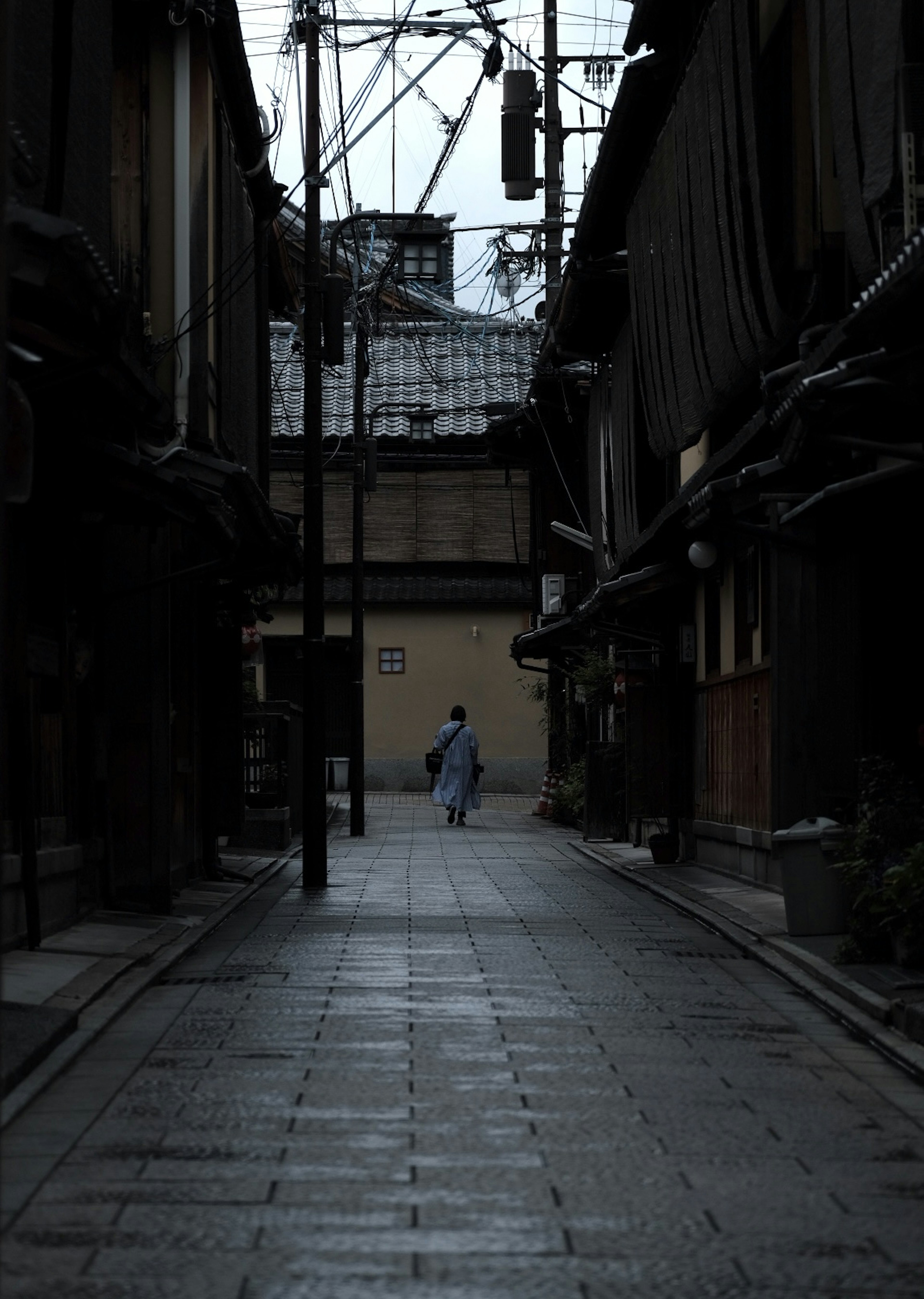 A person in a kimono walking down a quiet alley with a dark background