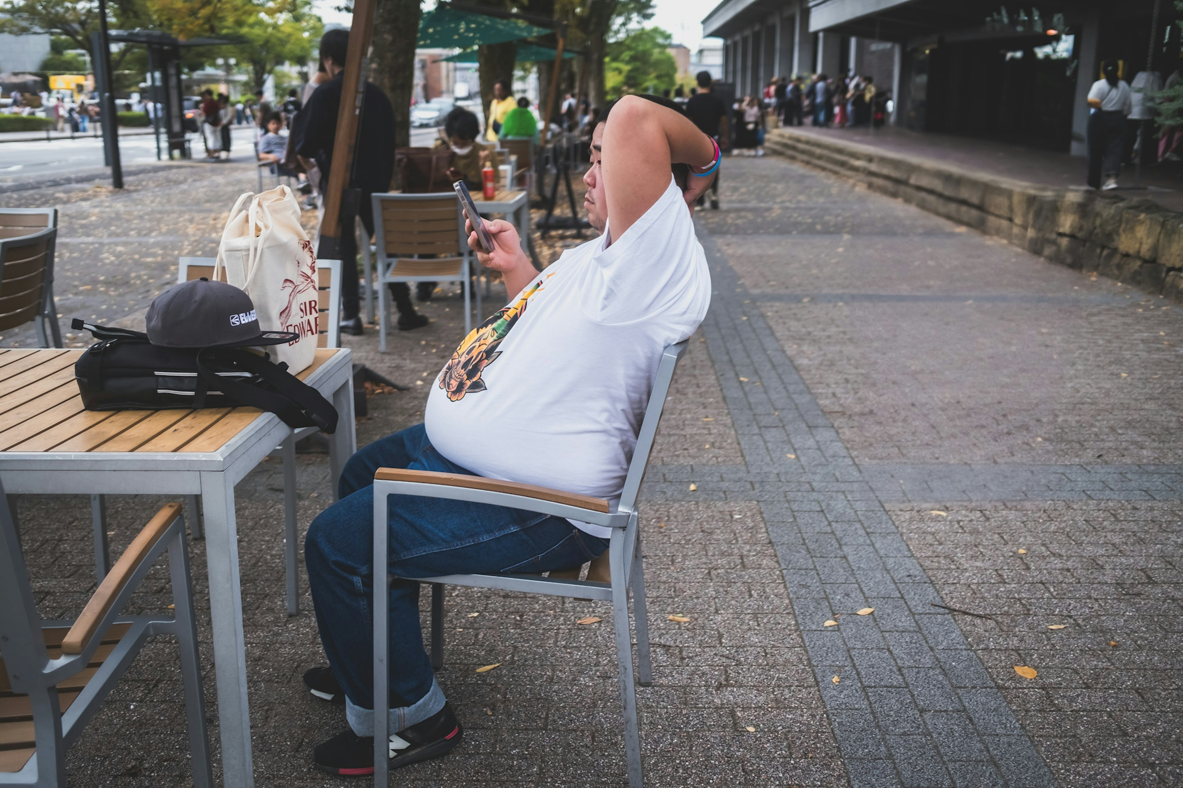 公園のベンチに座っている太った男性がスマートフォンを操作している