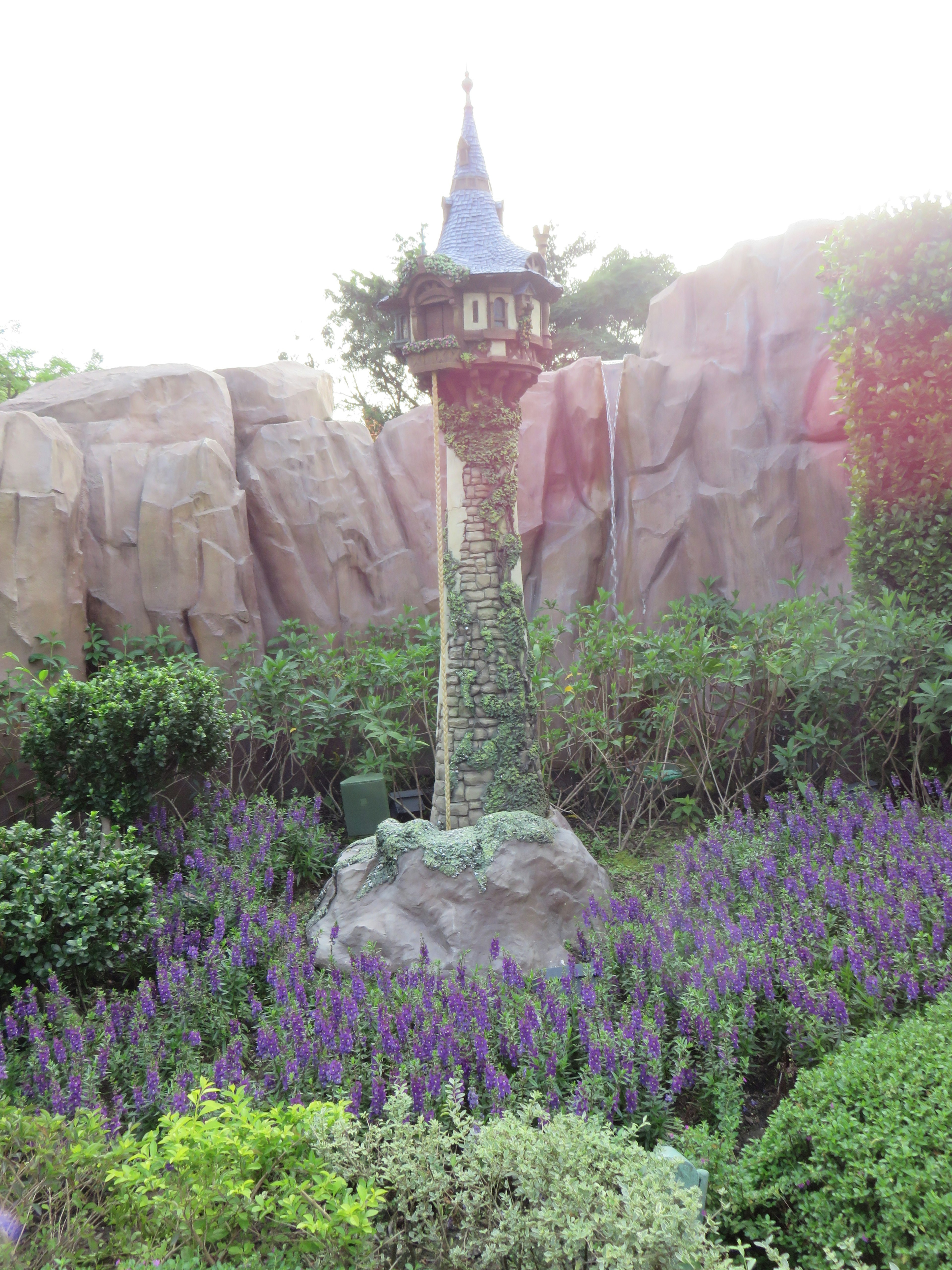 Estatua de torre rodeada de flores moradas y fondo rocoso