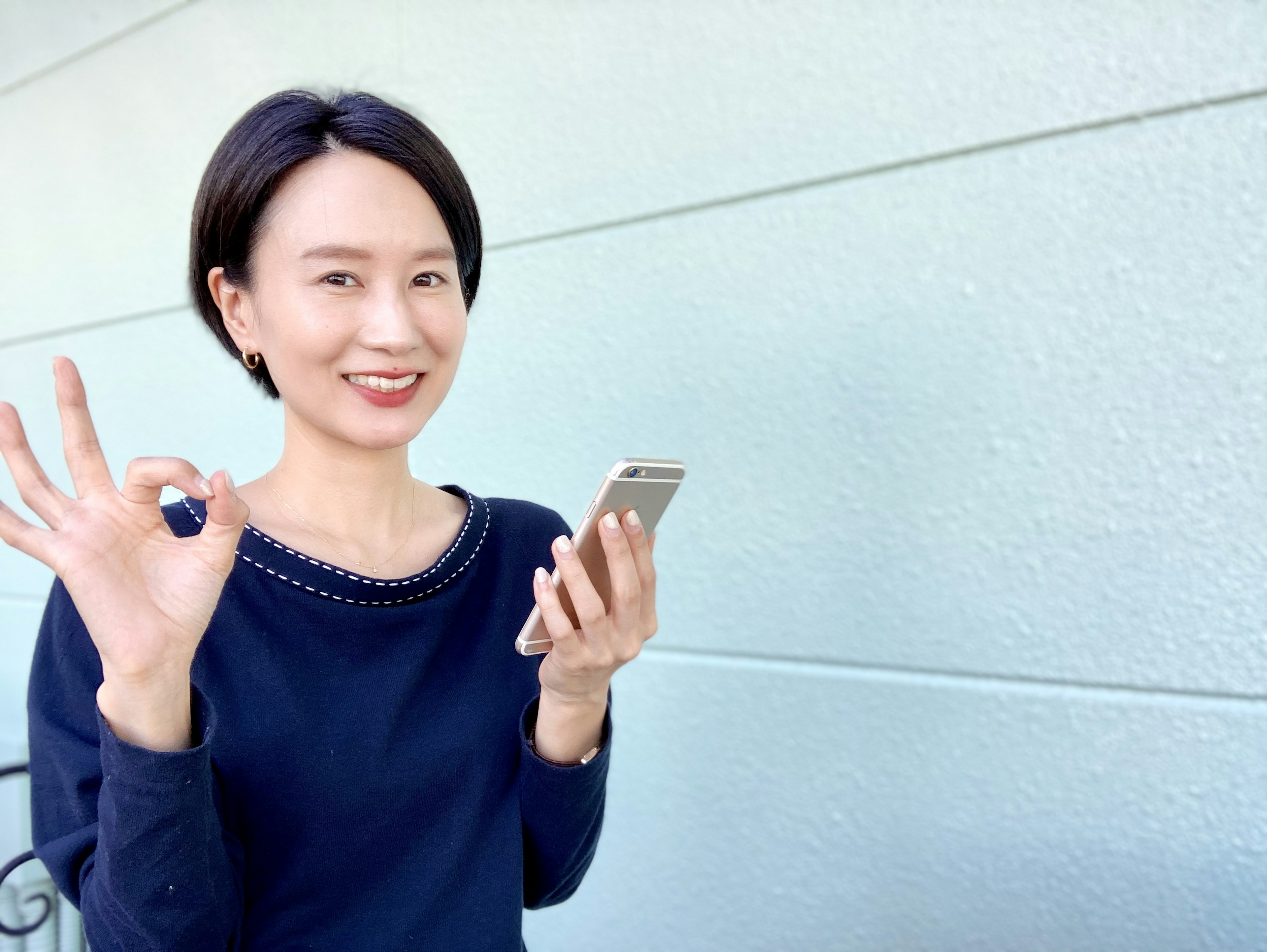 Mujer sonriendo y haciendo el signo OK mientras sostiene un teléfono inteligente