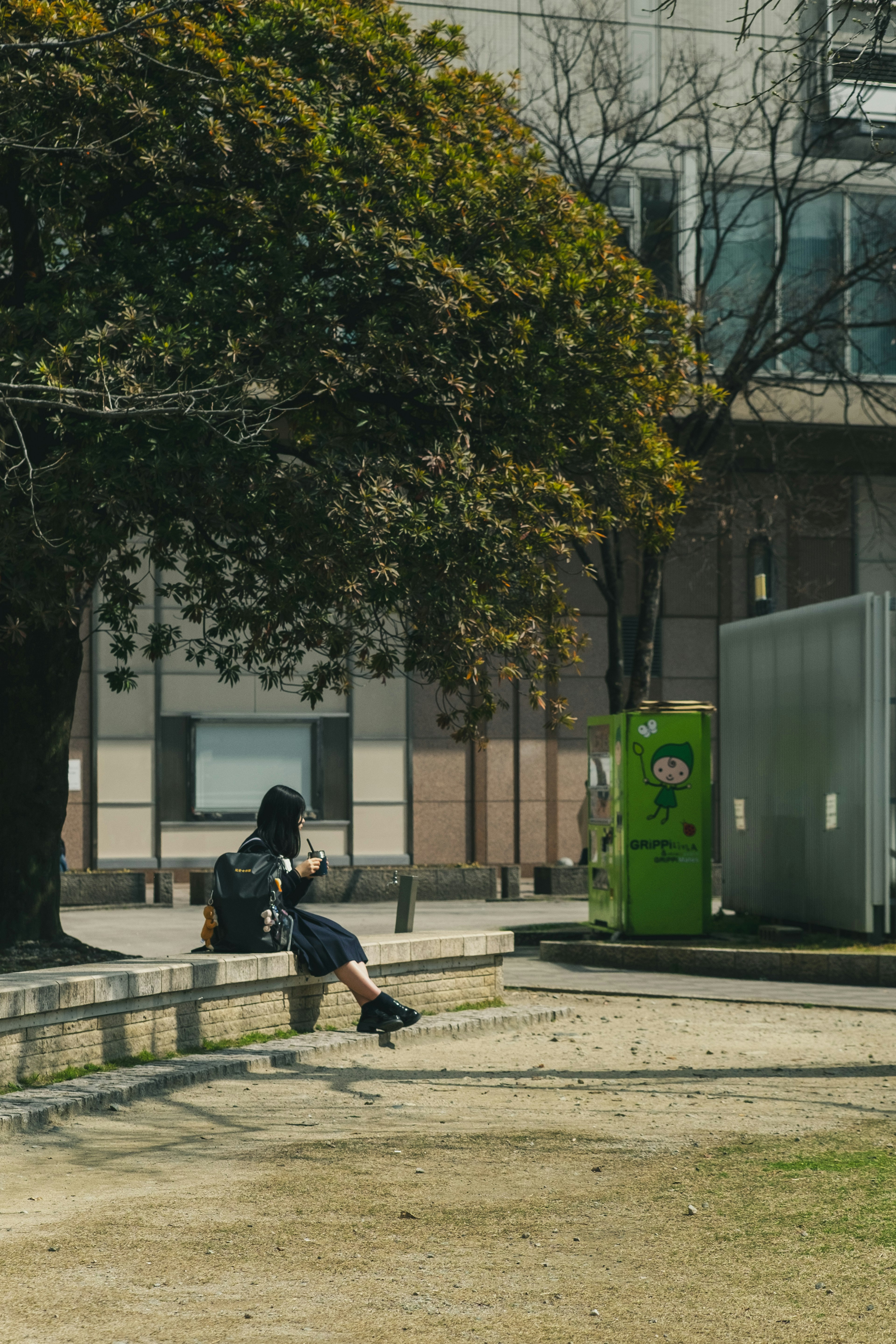 Woman sitting on a park bench with a green trash bin