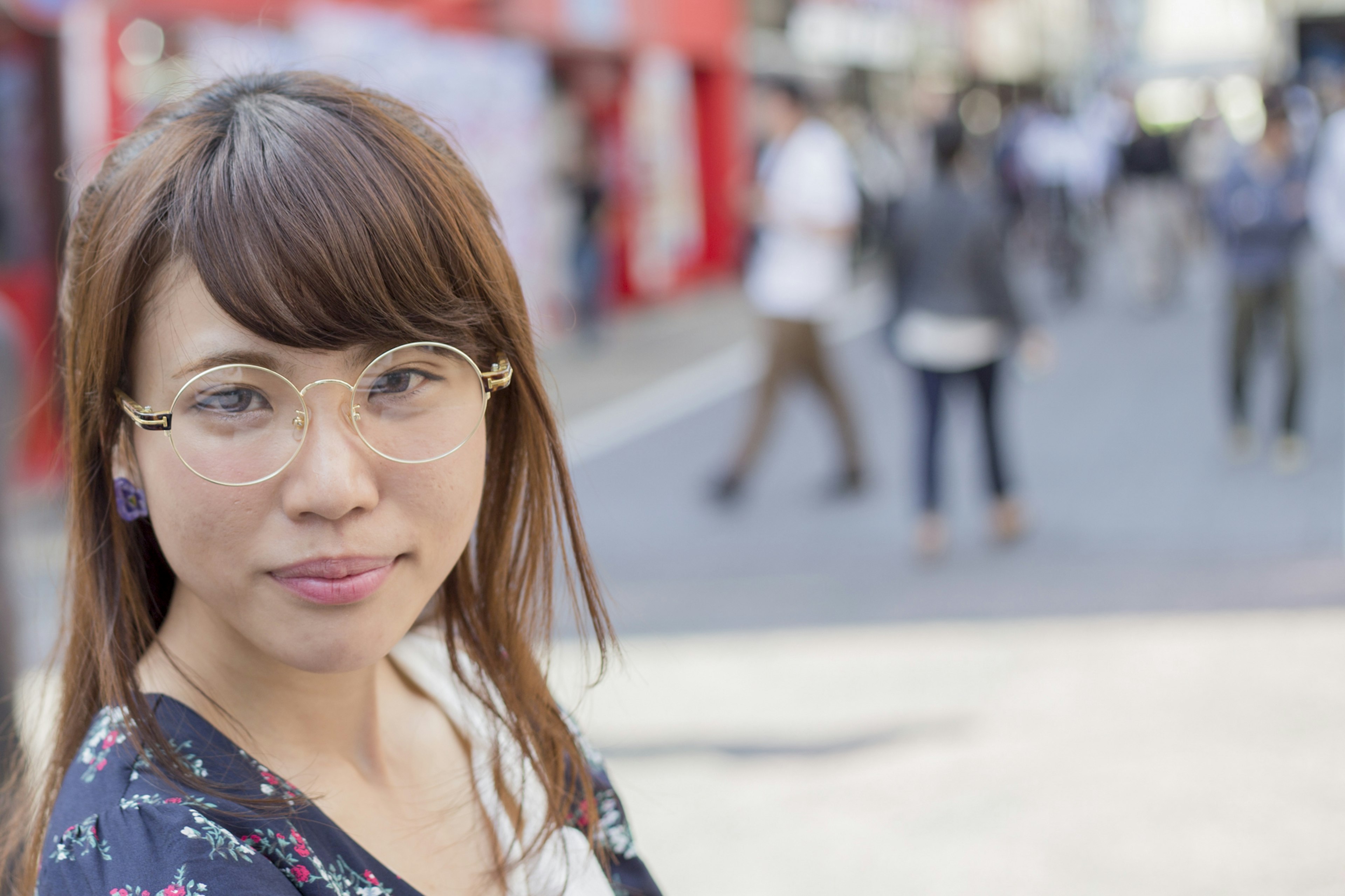 Portrait d'une femme souriante dans la rue portant des lunettes avec de longs cheveux et des gens marchant en arrière-plan