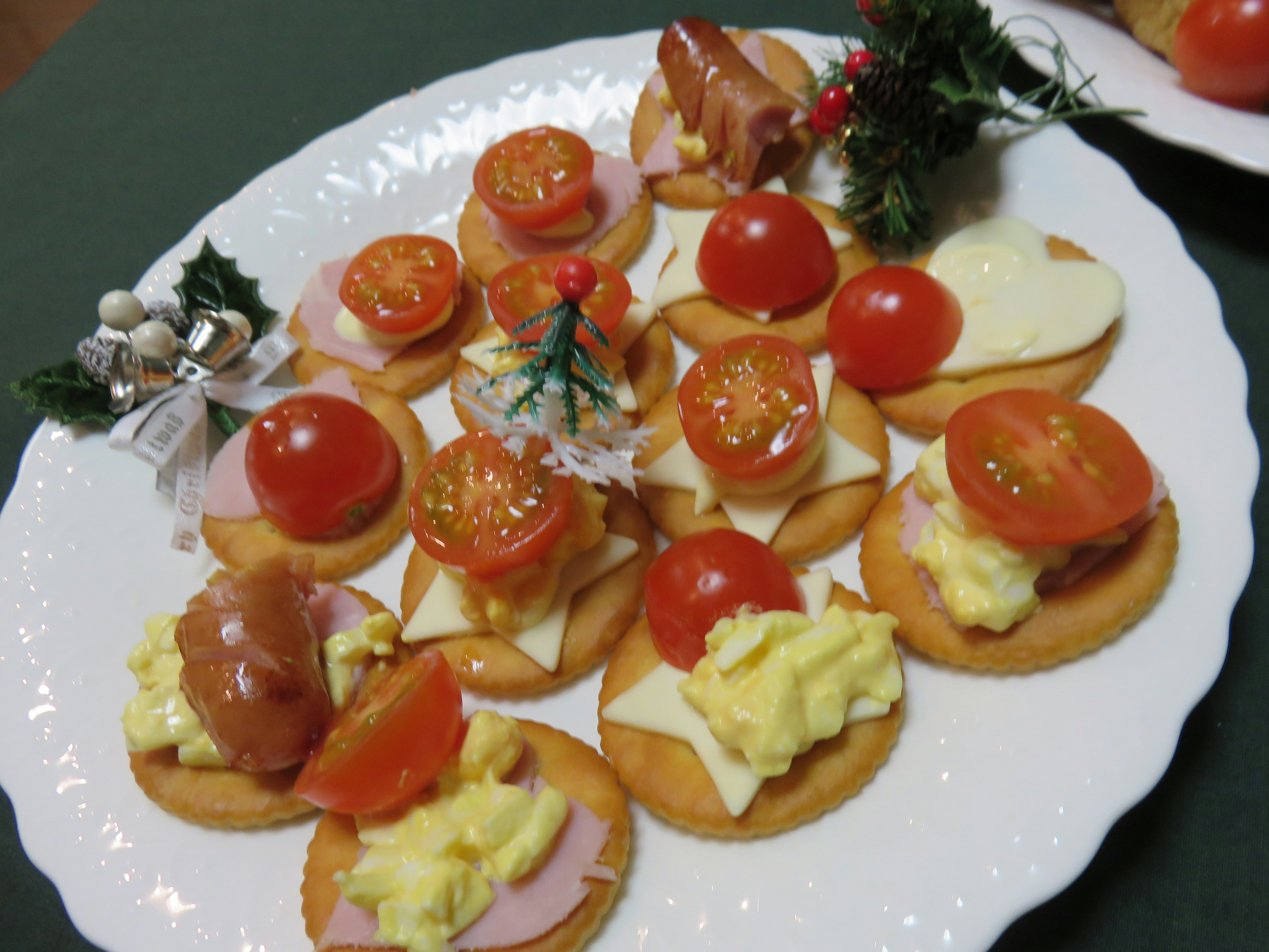 Plato de aperitivos navideños con galletas cubiertas de tomates jamón queso y crema