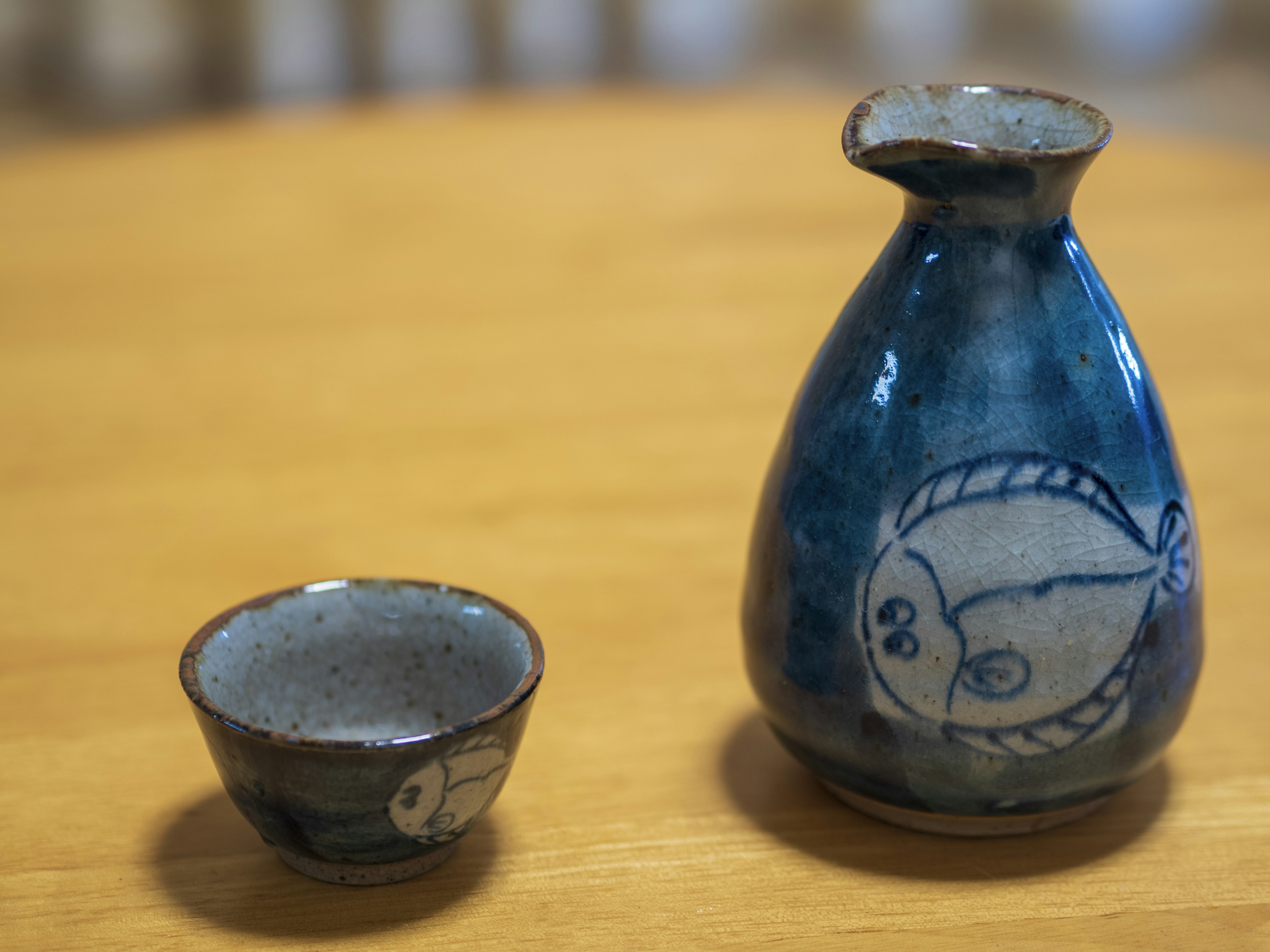 Una bottiglia di sake in ceramica blu e una piccola tazza sono posate su un tavolo di legno