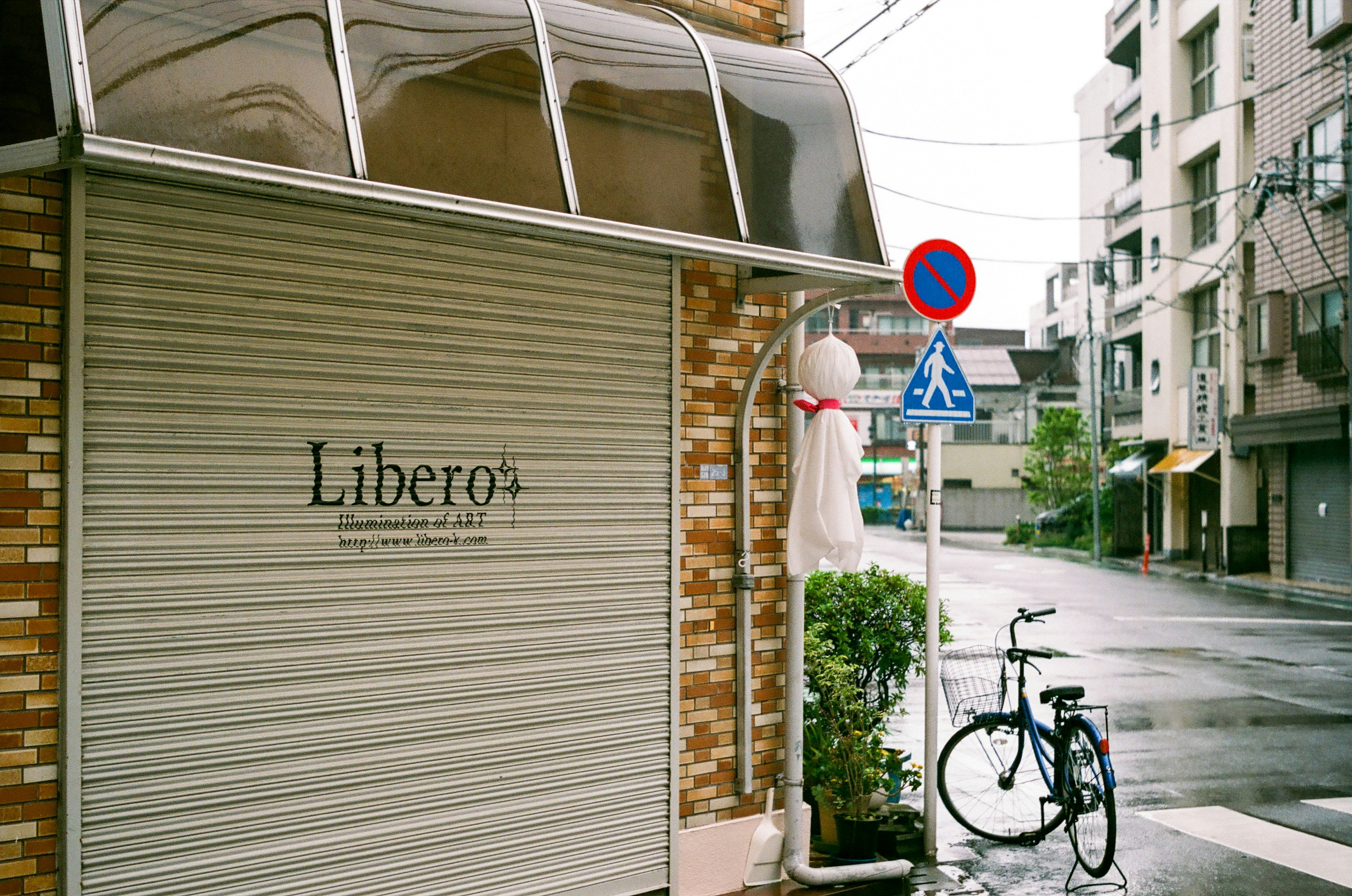 Fachada de la tienda Libero en una esquina lluviosa con una bicicleta