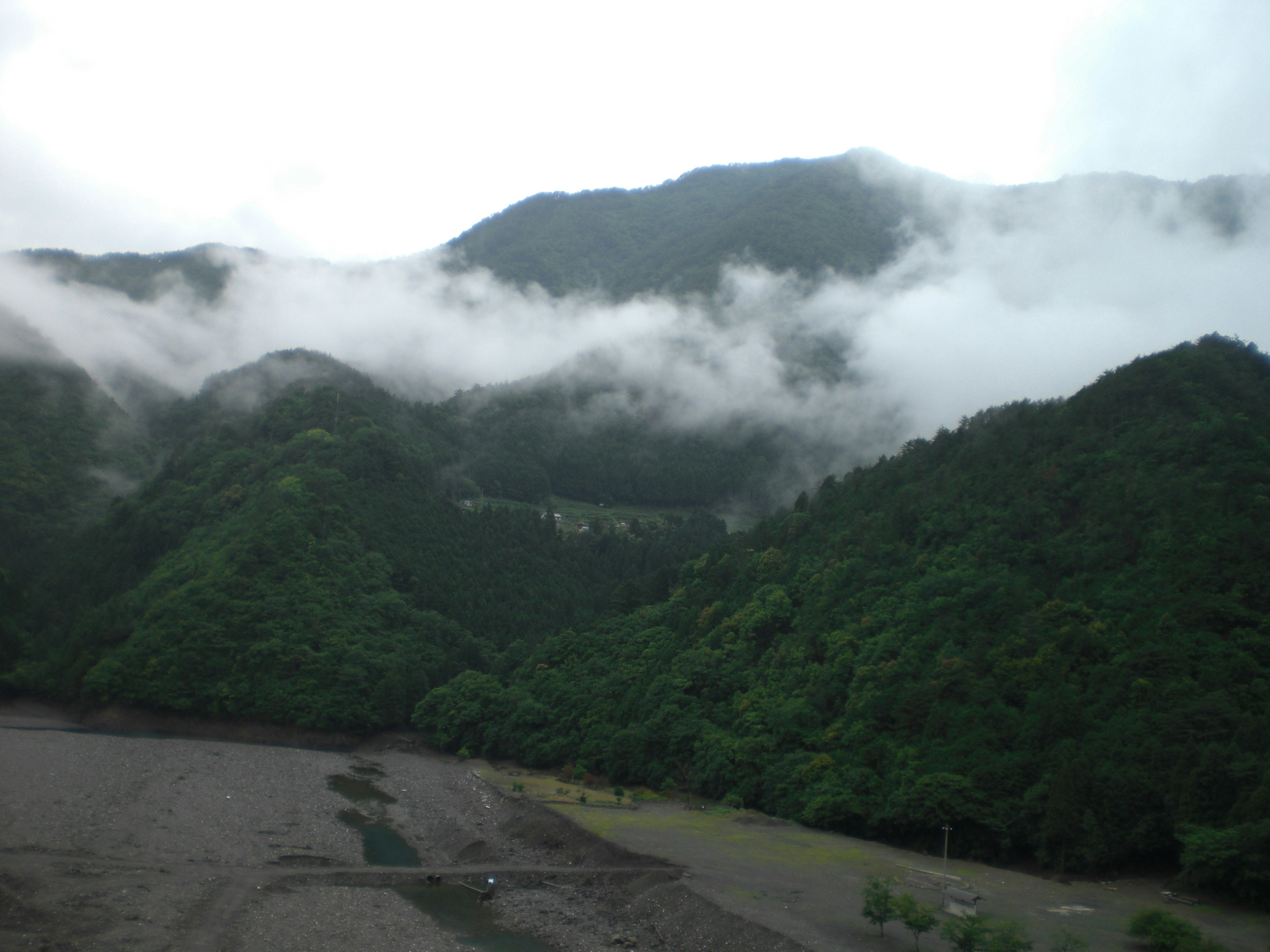 Montañas verdes cubiertas de niebla con un paisaje de tierra desnuda