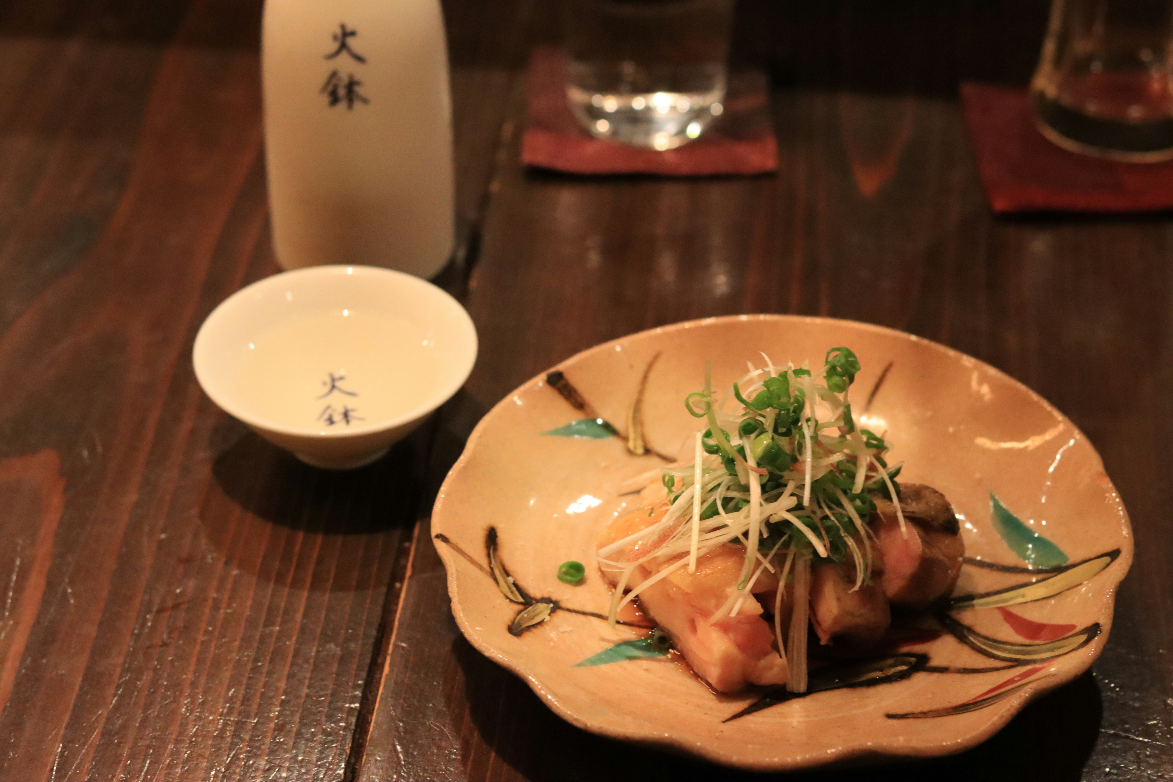 A beautifully decorated dish with food and a sake bottle on a wooden table