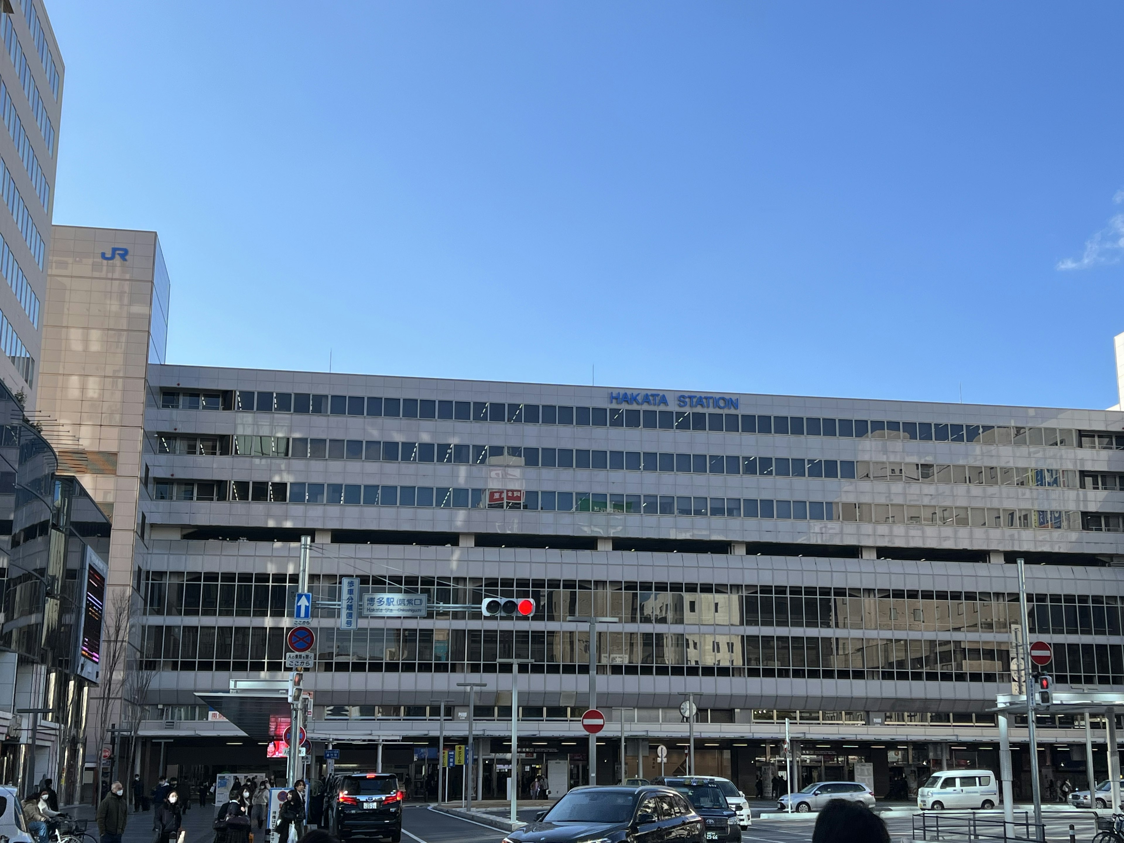 Façade d'un bâtiment moderne sous un ciel bleu avec des feux de circulation et des voitures