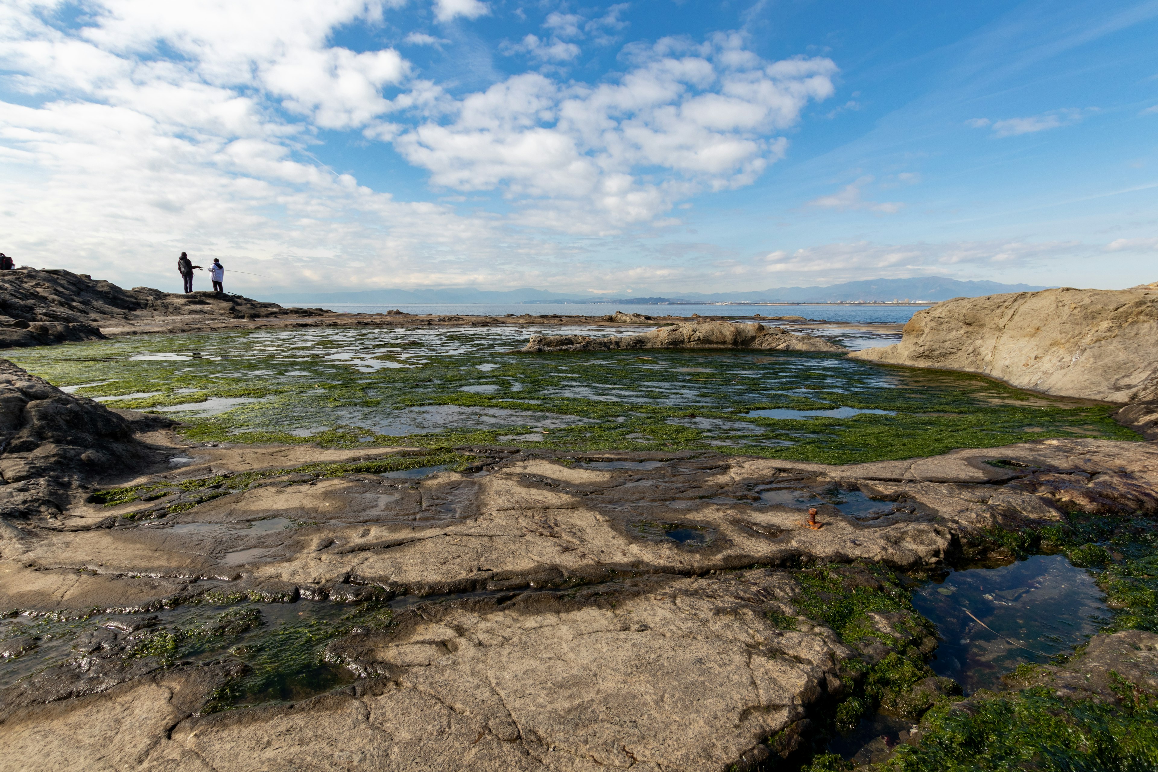 Persone in piedi su una costa rocciosa con cielo blu