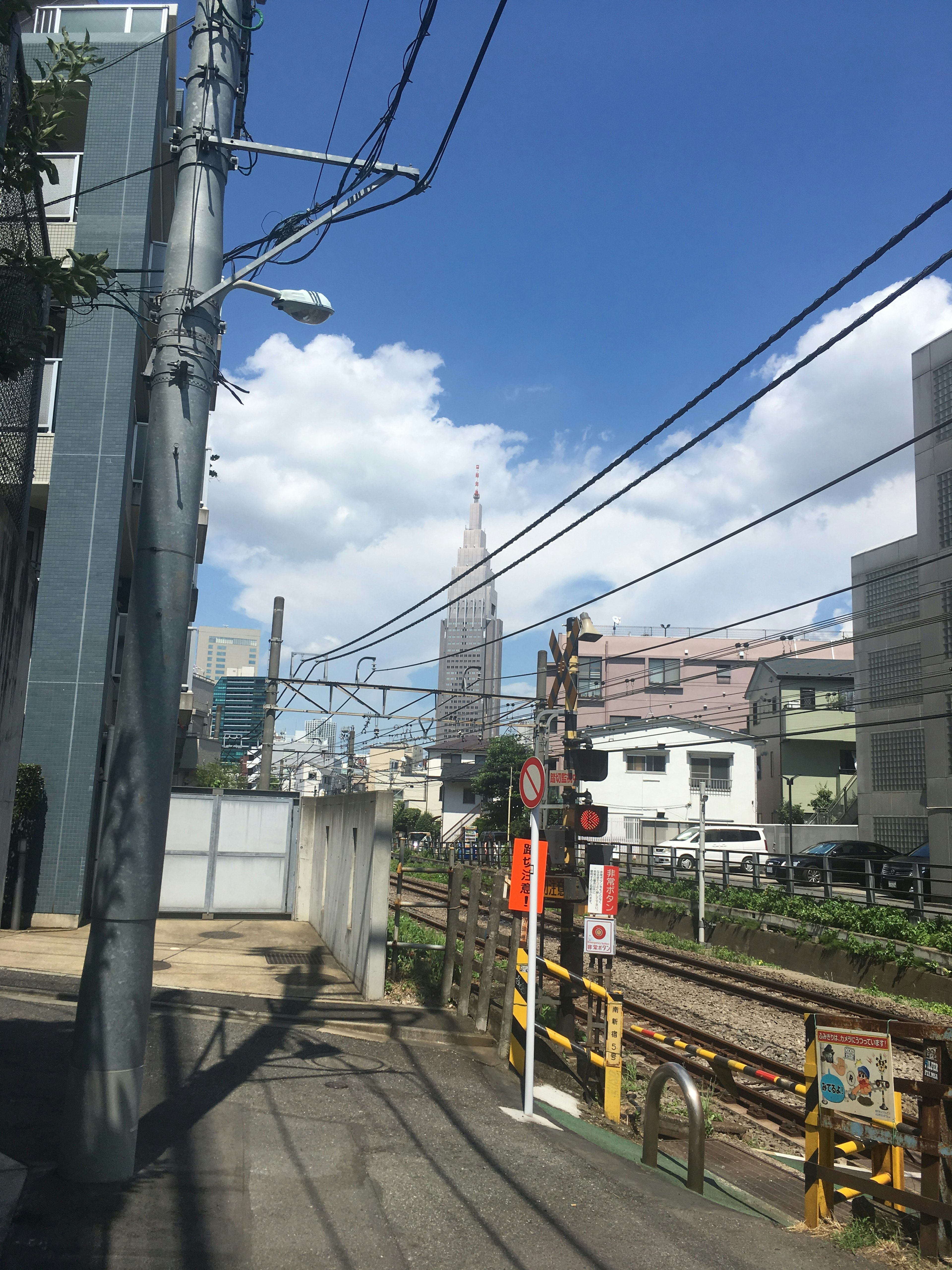 Paisaje urbano cerca de una estación de tren con cielo azul y nubes, vías y líneas eléctricas visibles