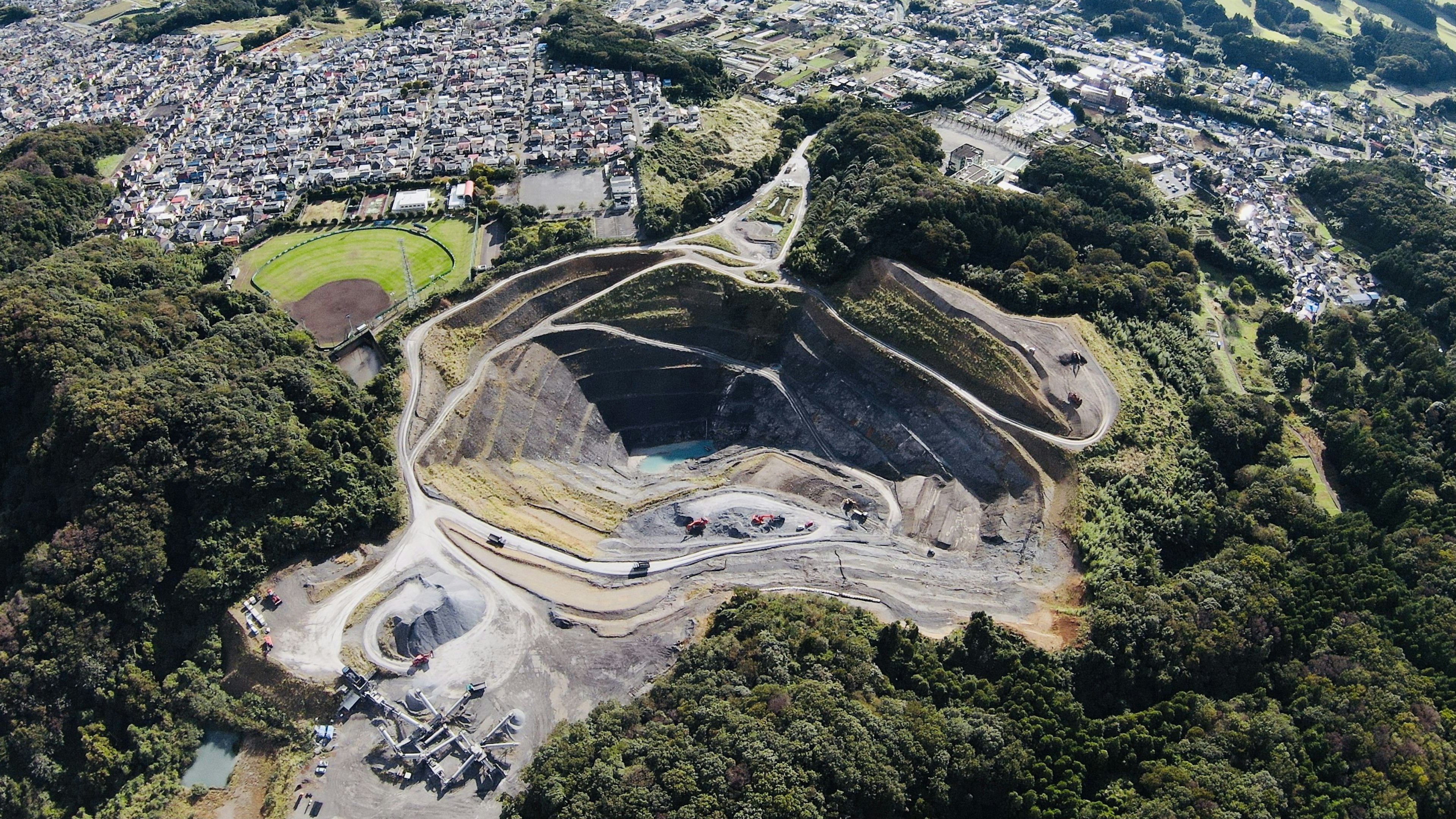 Aerial view of a quarry with terraced slopes surrounded by residential areas and greenery