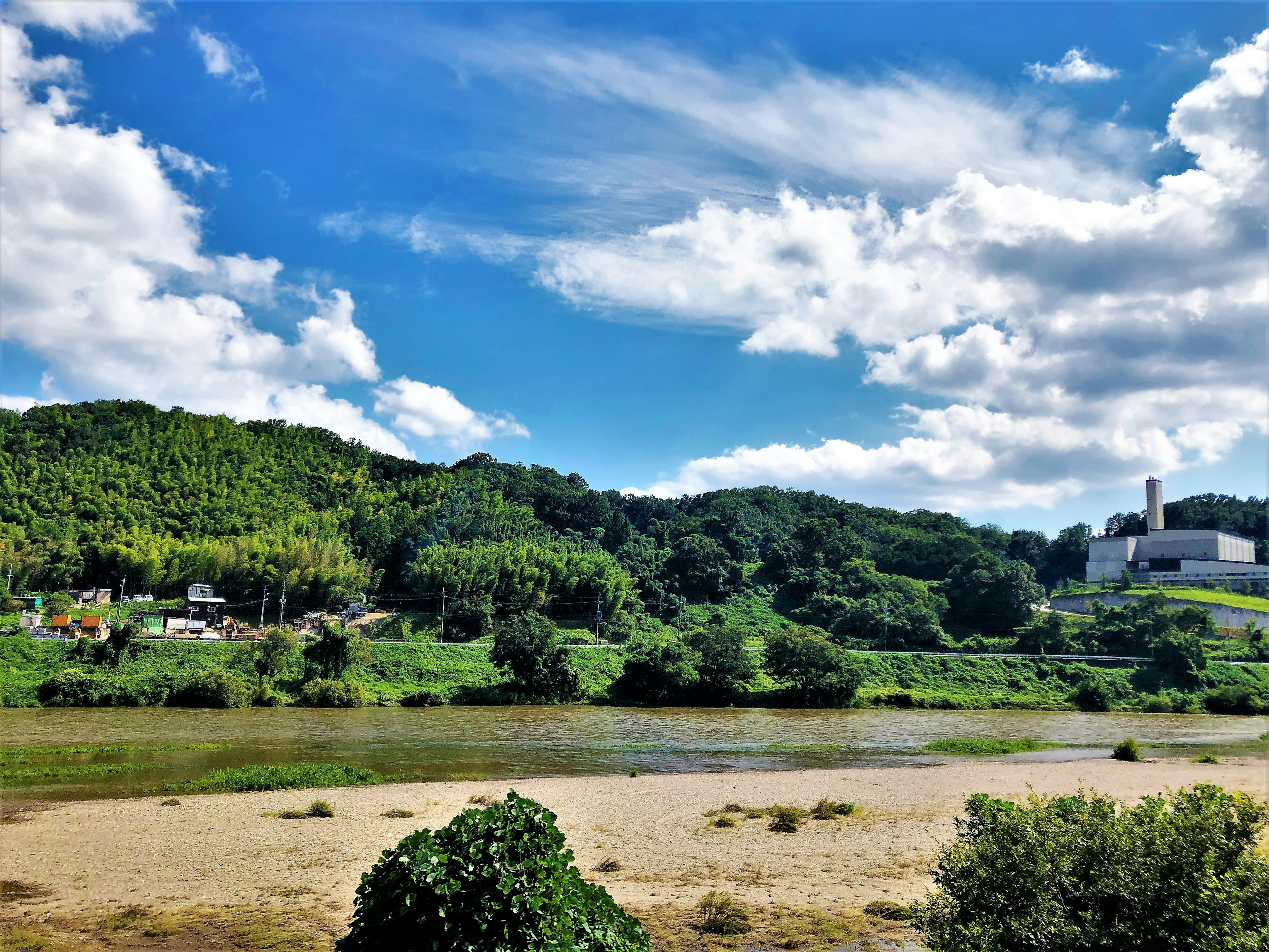 Vue pittoresque de collines verdoyantes et d'une rivière sous un ciel bleu avec des nuages blancs