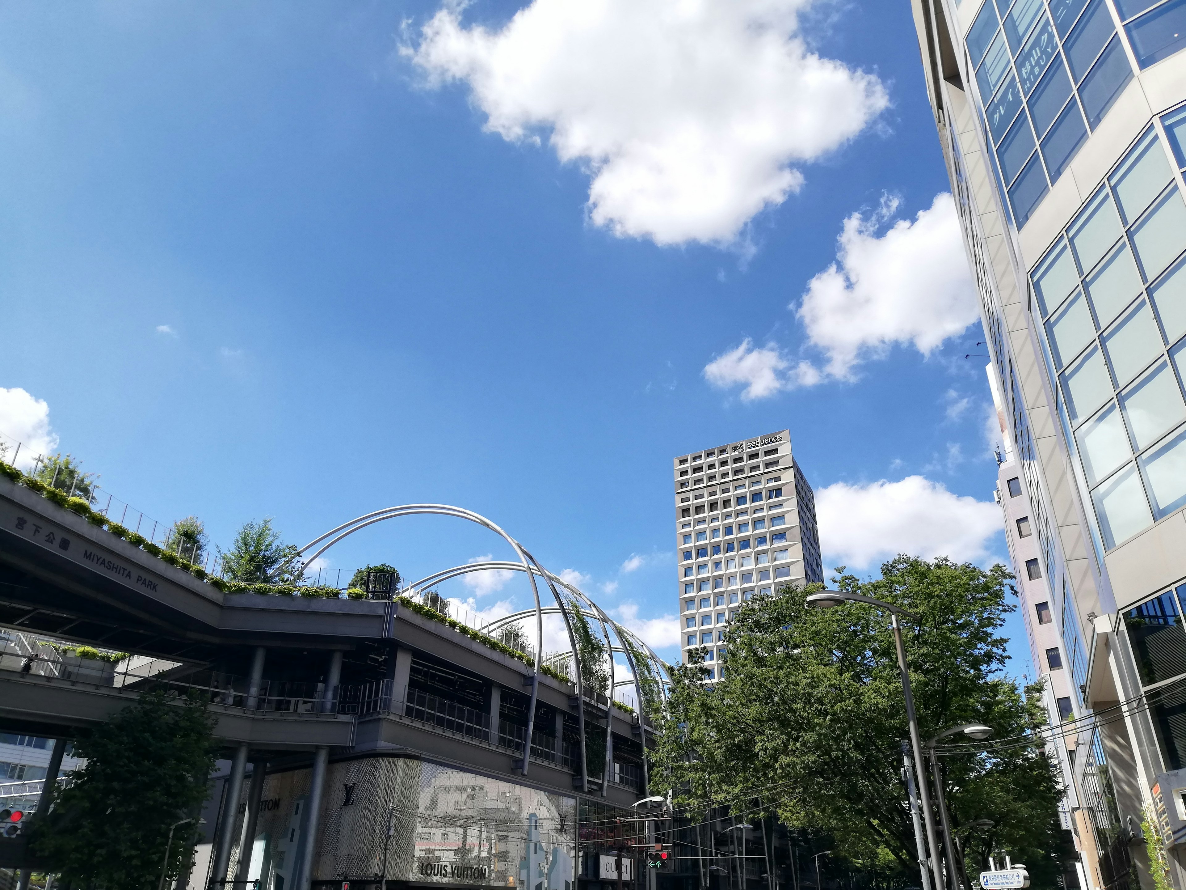 Urban landscape featuring skyscrapers and lush greenery under a blue sky with white clouds