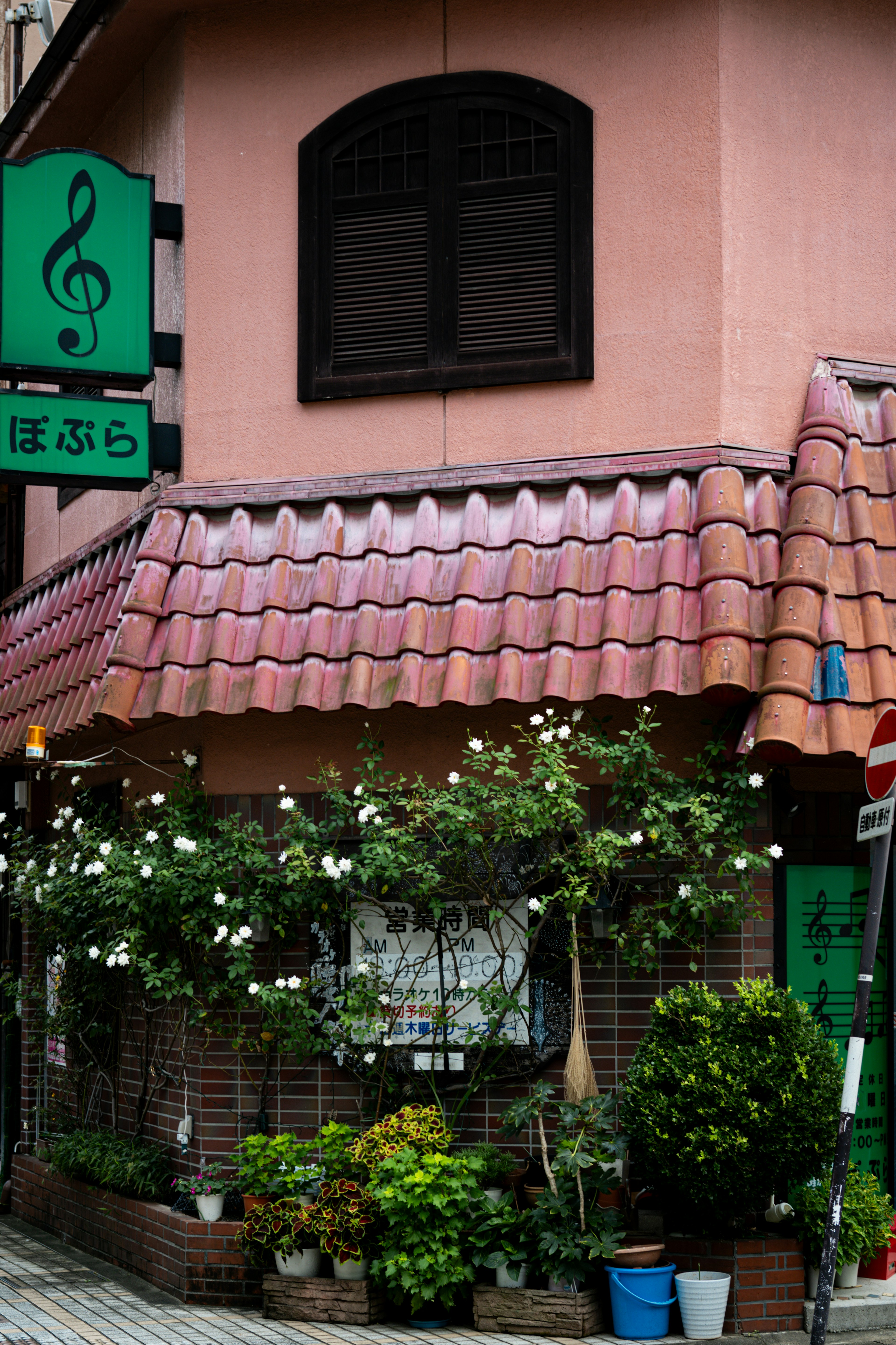 ピンクの壁と赤い瓦屋根の小さな建物 植木鉢に花が咲いている 音符の看板が特徴的