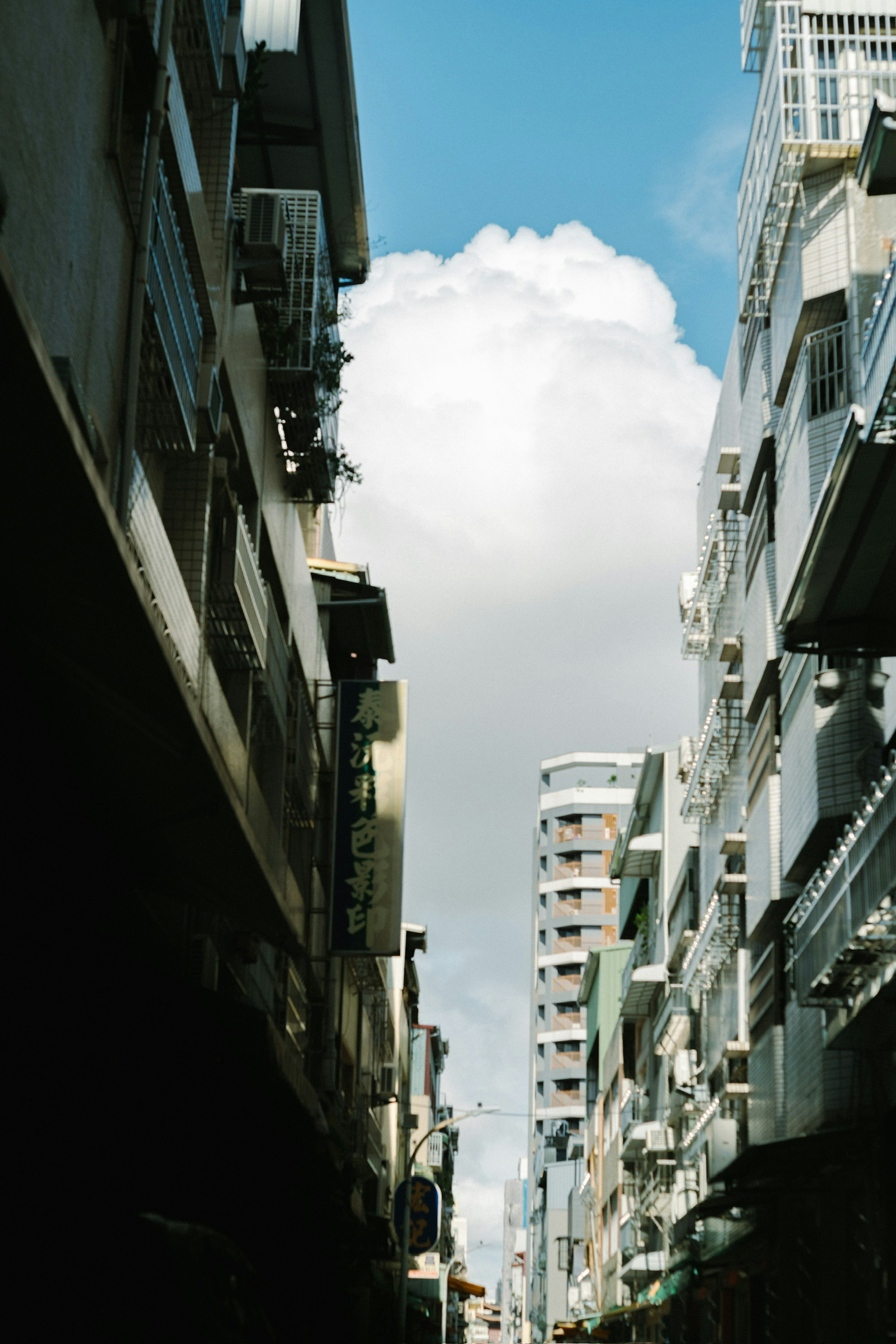 Calle estrecha flanqueada por edificios altos y una nube en el cielo azul