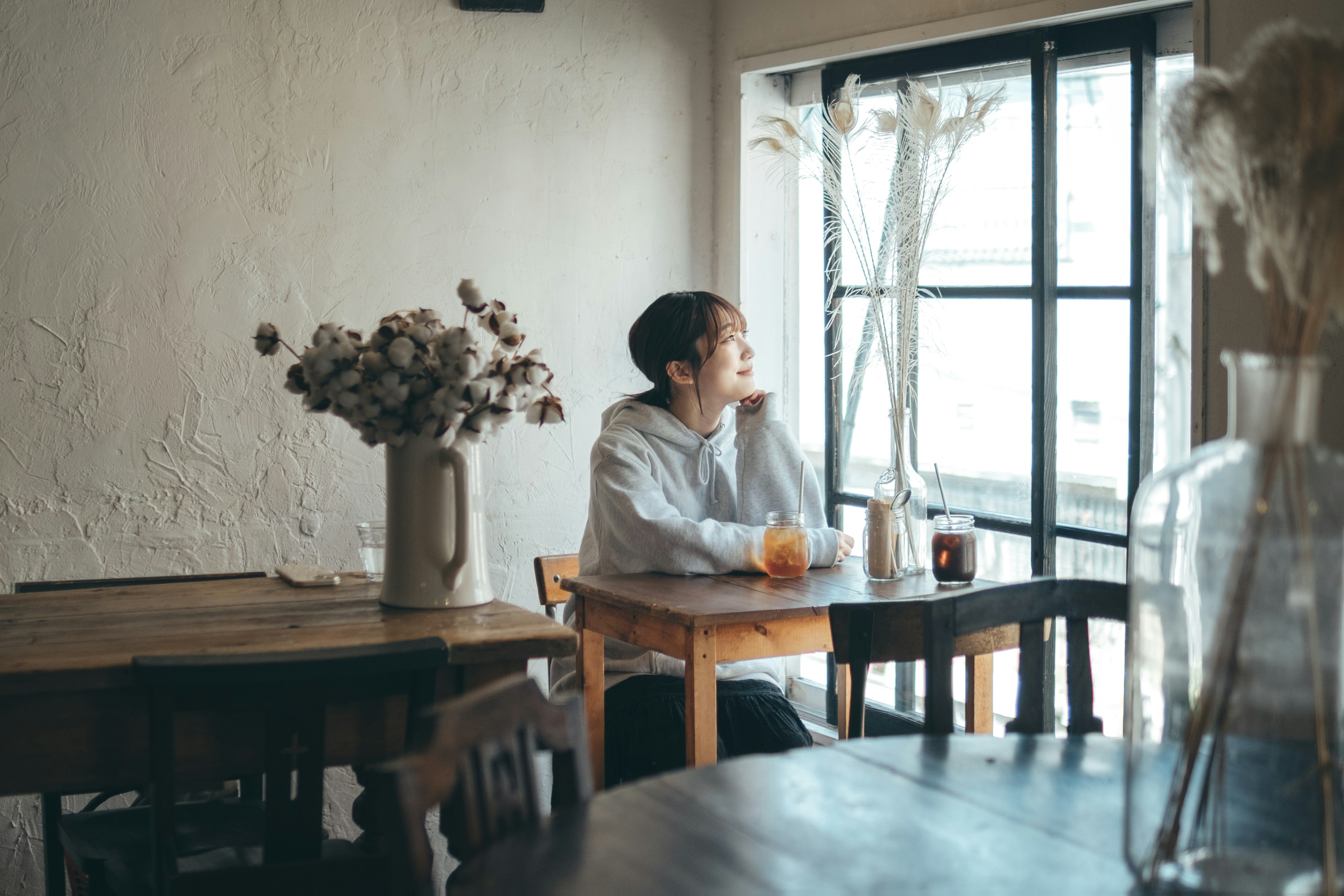 窓のそばで飲み物を楽しむ男性とドライフラワーのあるカフェの内部