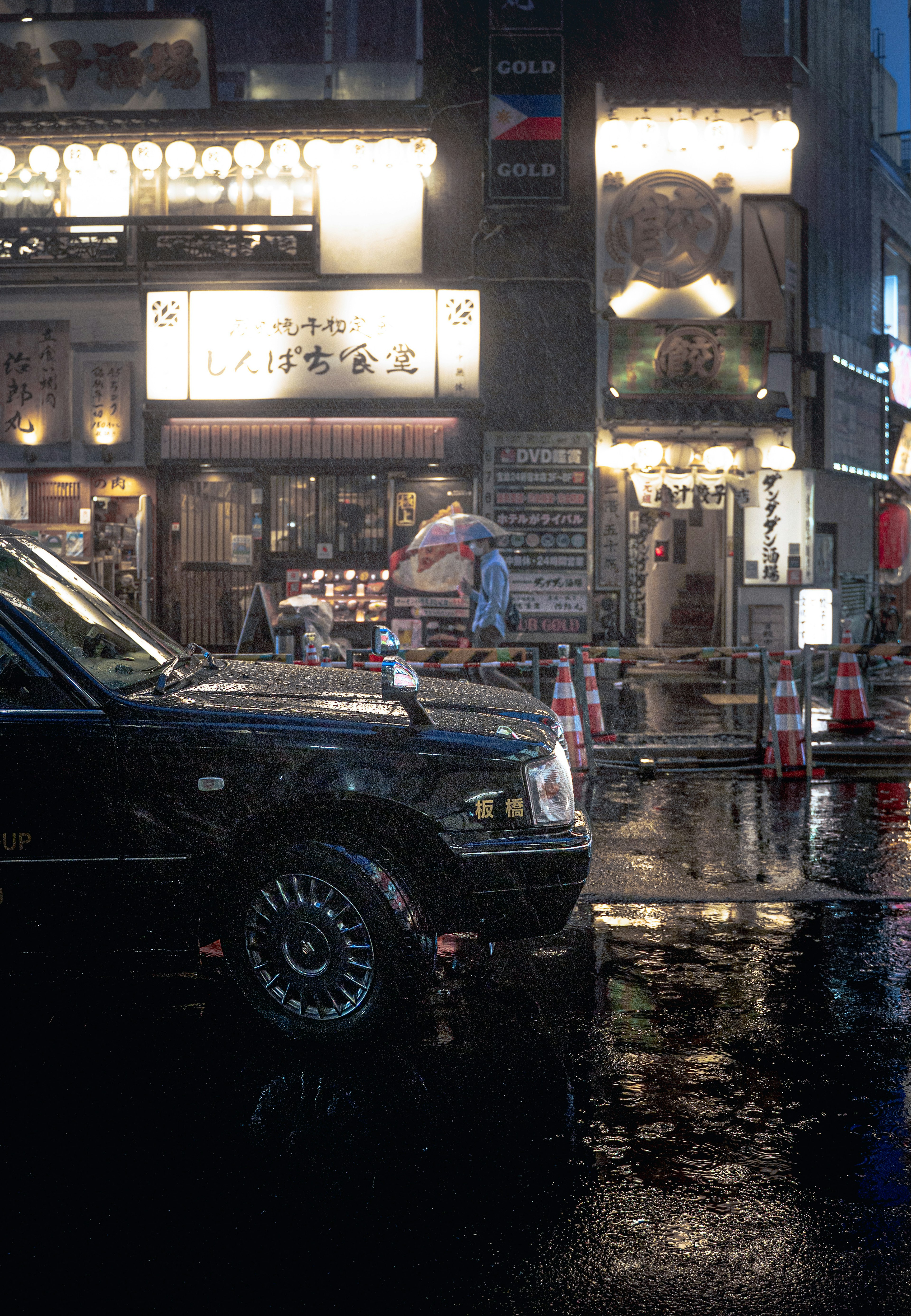 A black car on a rainy street with bright signs and shops