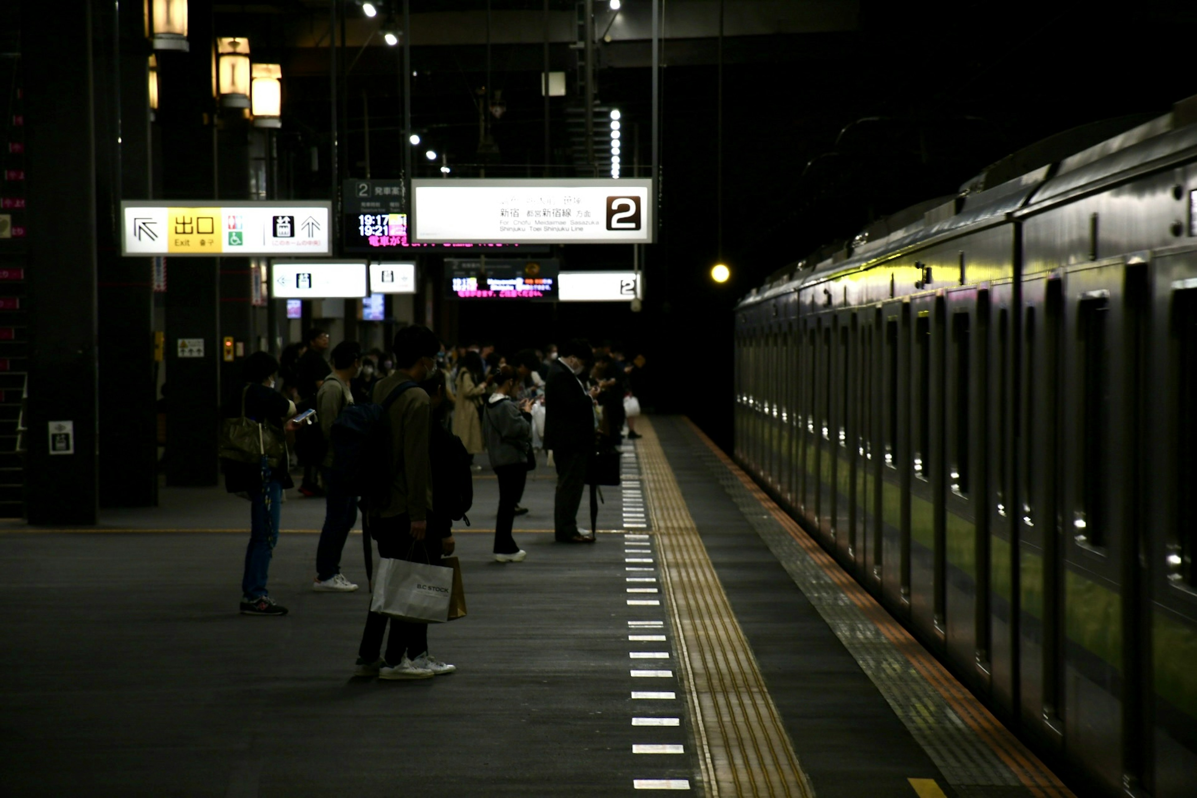 夜の駅で電車を待つ乗客たちと明るい看板