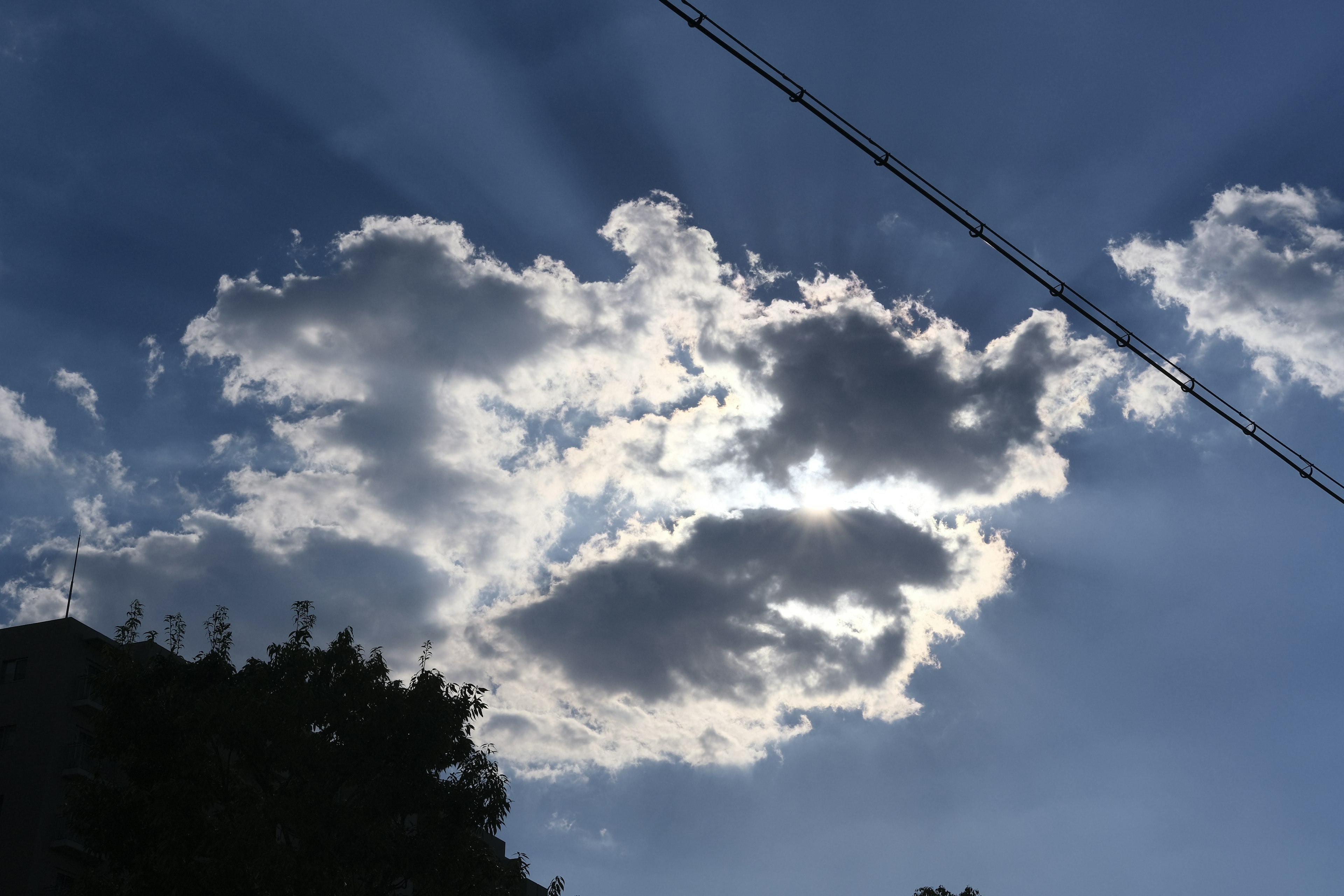 Weiße Wolken breiten sich über einem blauen Himmel aus, während Sonnenlicht hindurchscheint