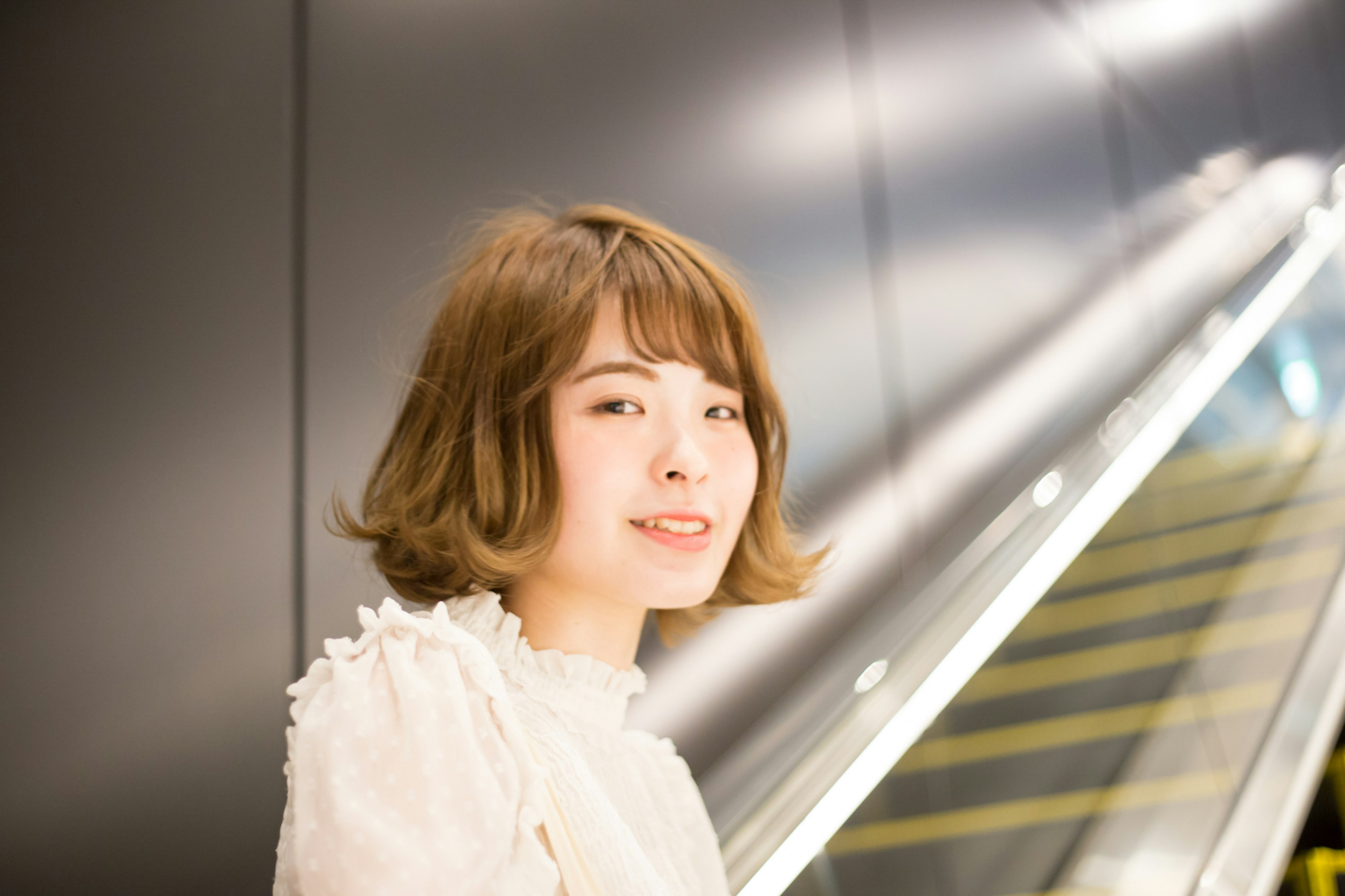 Young woman standing by an escalator wearing a white blouse with short hair