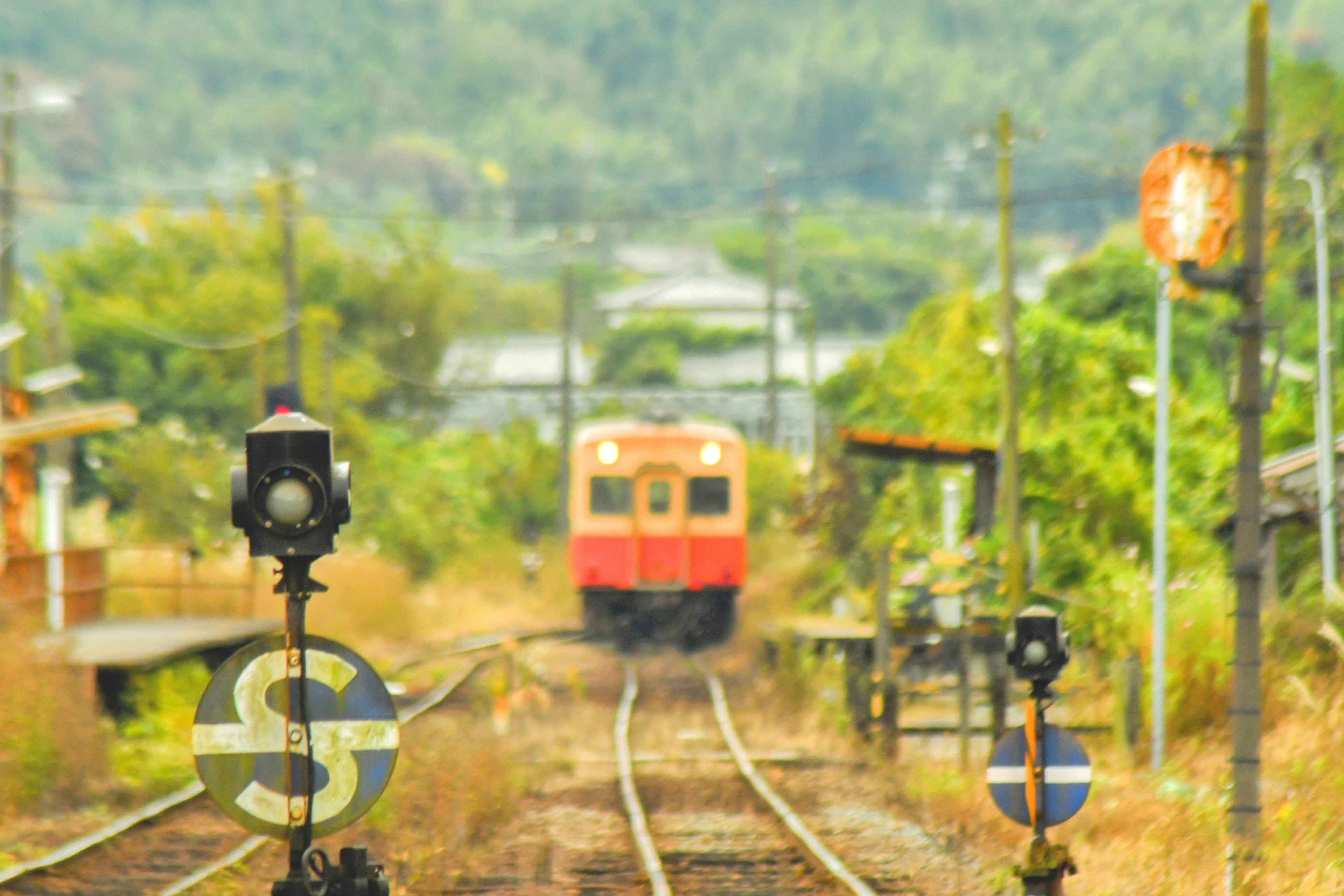 Rural railway scene with a red train approaching railway signals and tracks