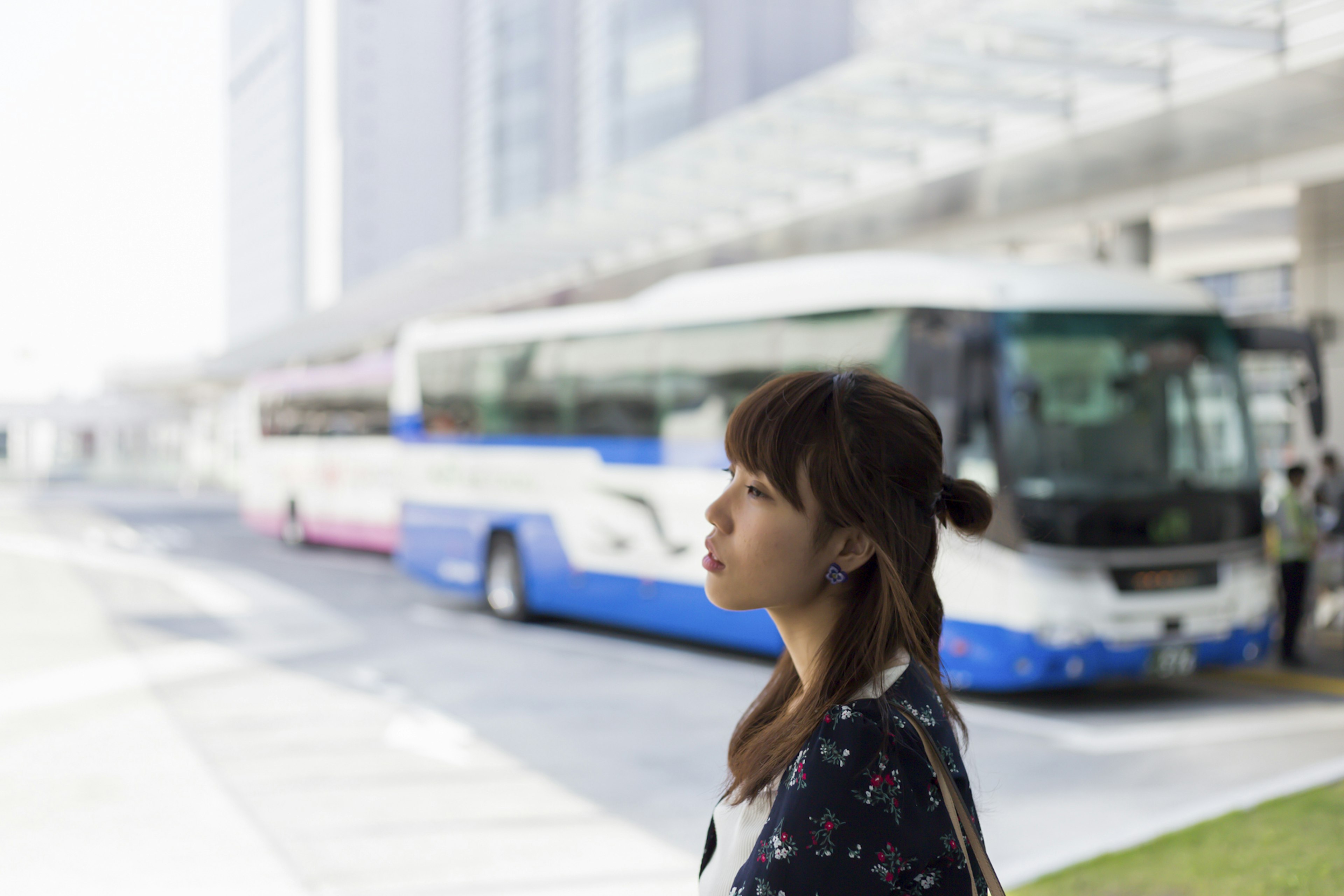 Perfil de una mujer esperando en una parada de autobús con autobuses al fondo