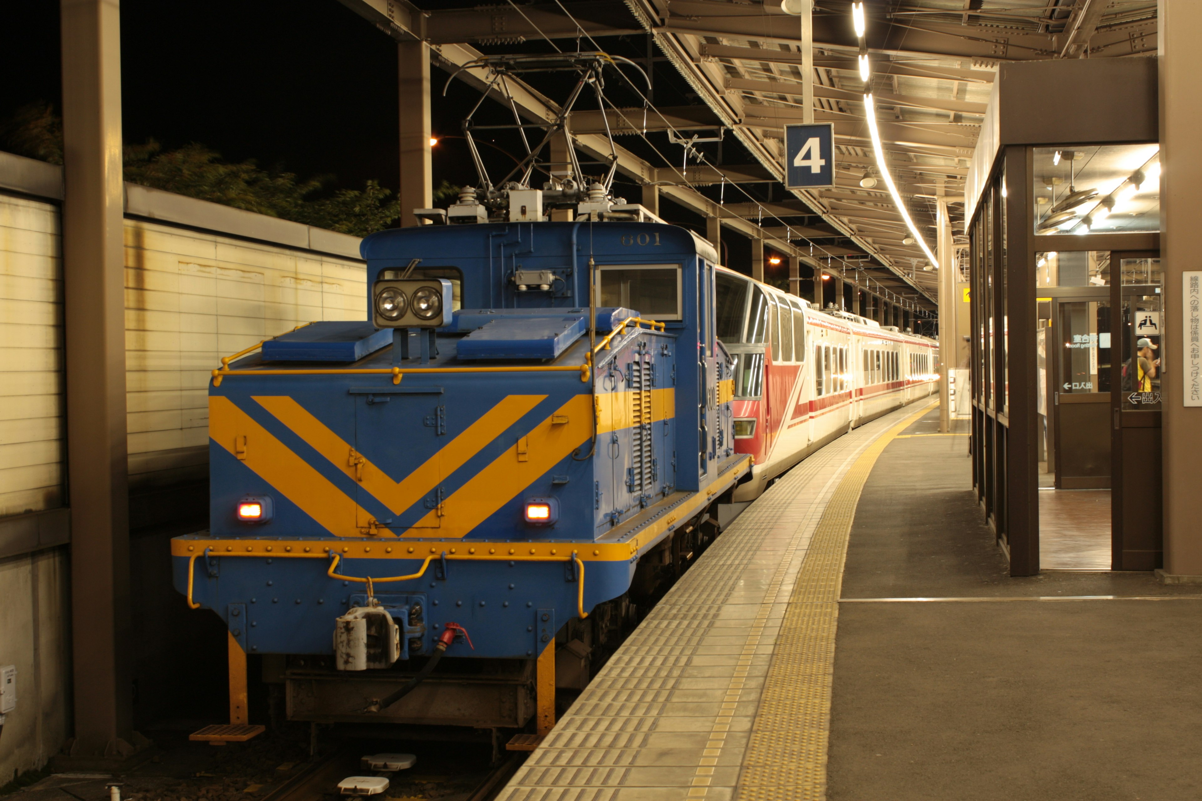 Lokomotif listrik biru yang diparkir di stasiun pada malam hari di samping kereta penumpang