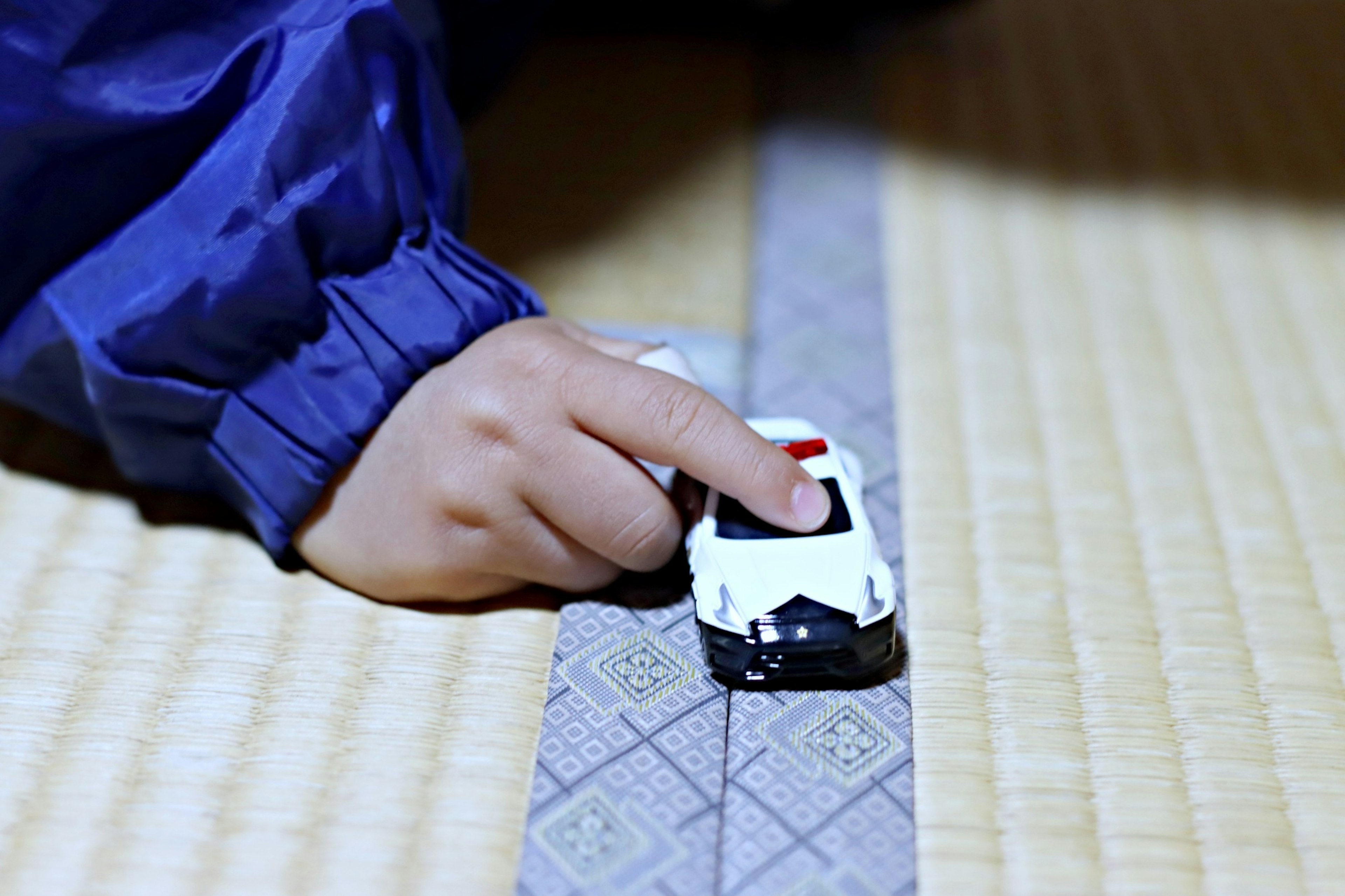 Une main d'enfant poussant une voiture jouet blanche sur un sol en tatami