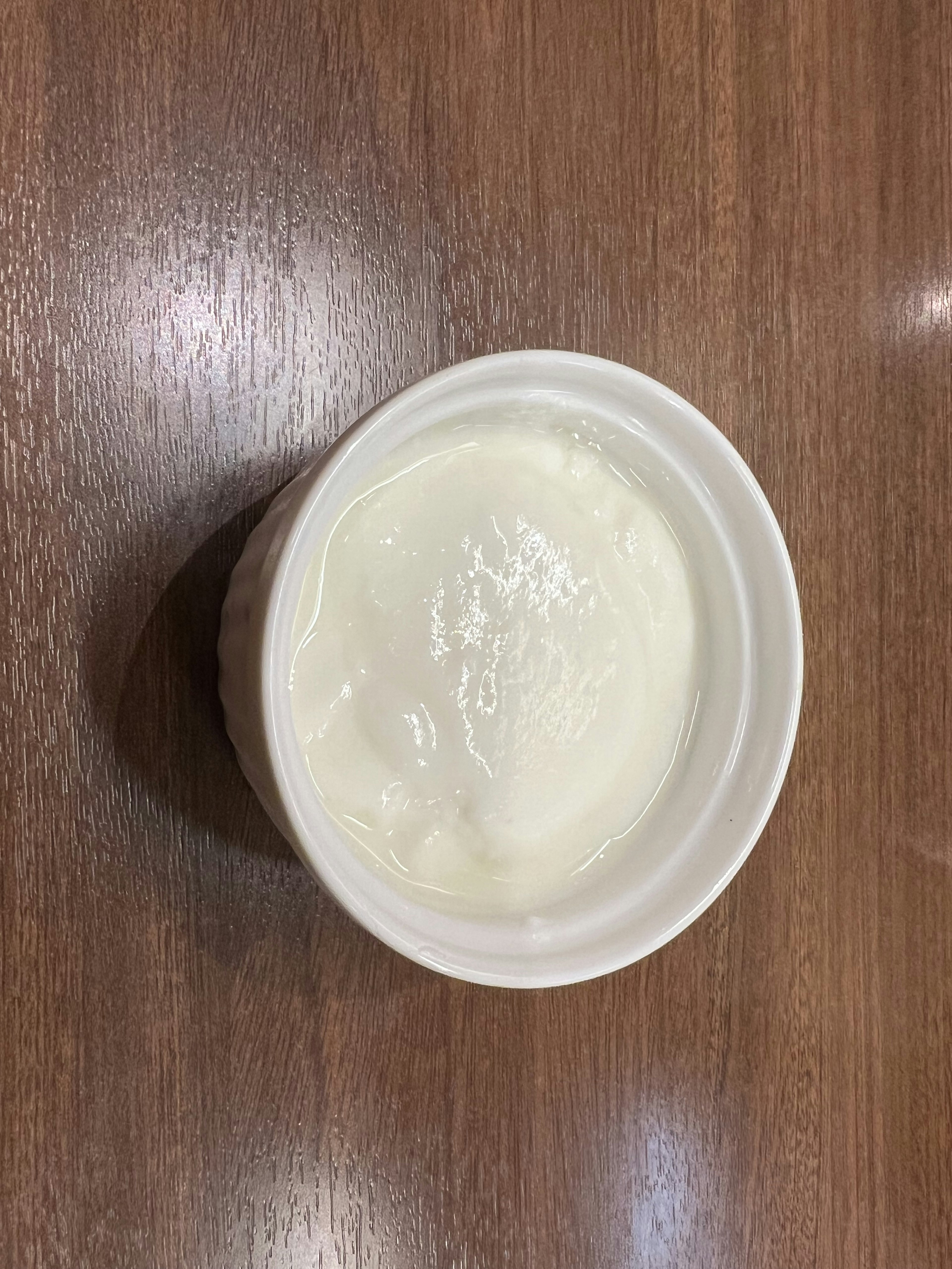 Close-up of a small cup containing white cream on a wooden surface