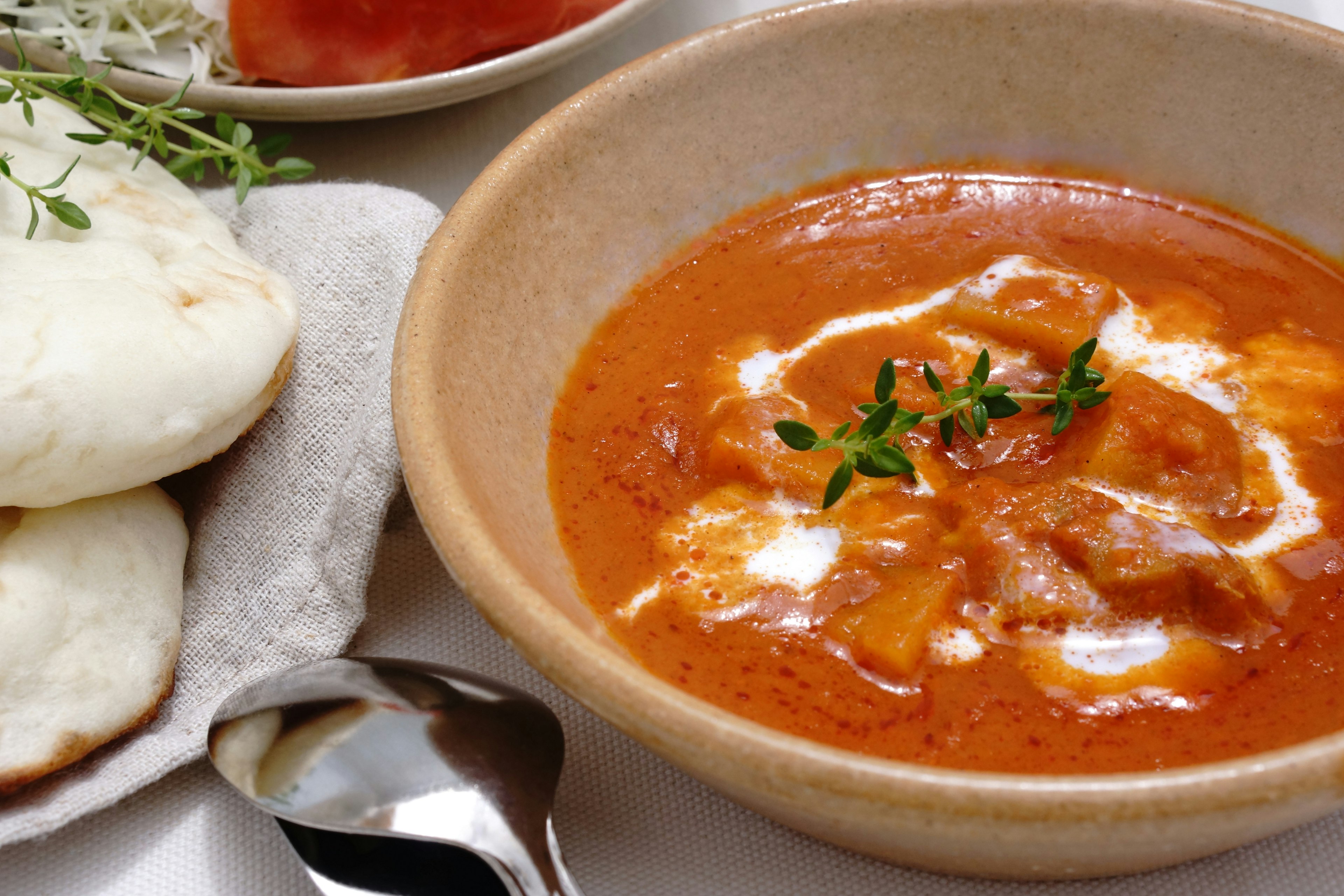 Bowl of creamy chicken curry with naan bread on the side