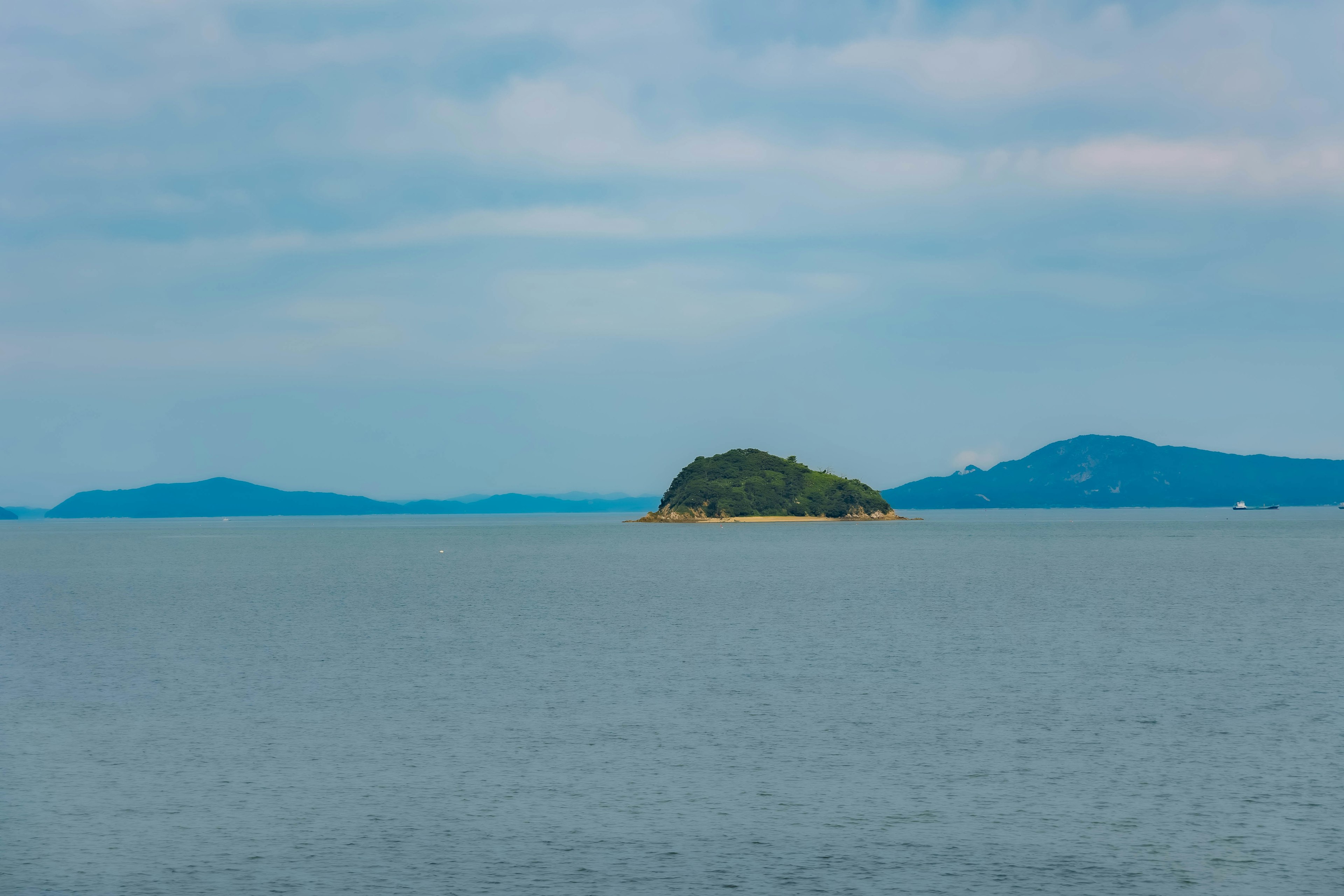 Serene view of the sea with a small island blue sky and calm water surface