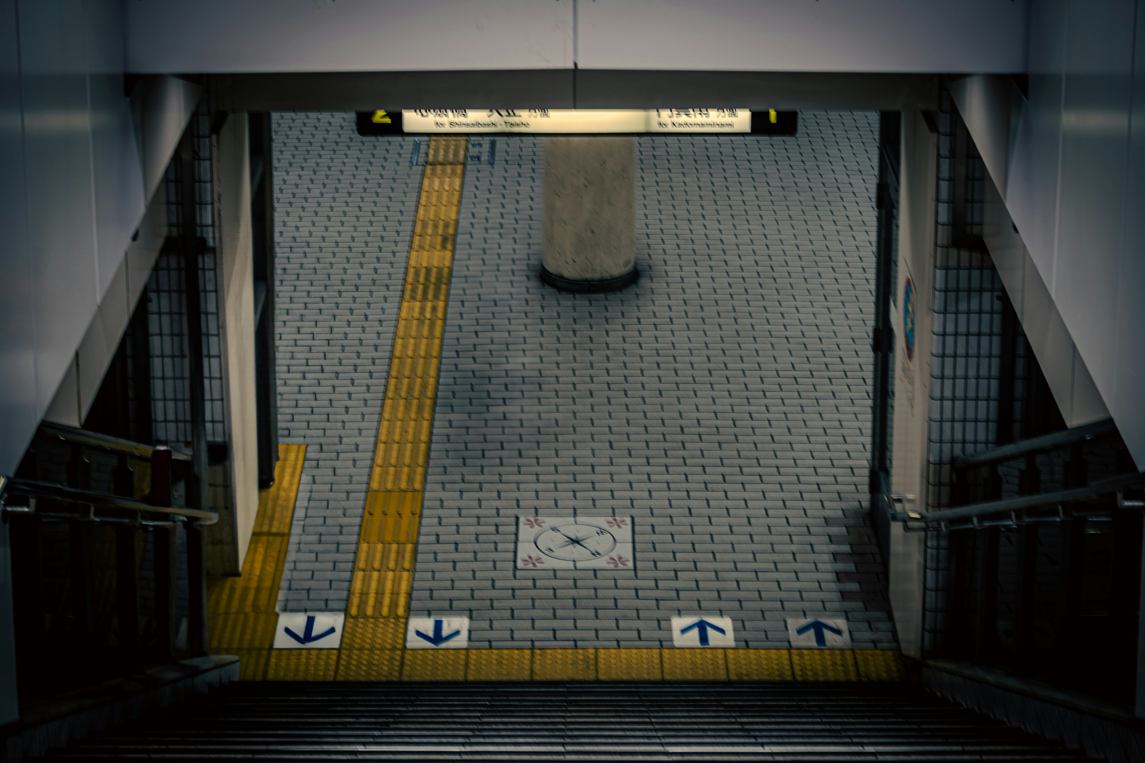 Vista de escaleras de metro y piso de baldosas con línea amarilla y marcadores direccionales