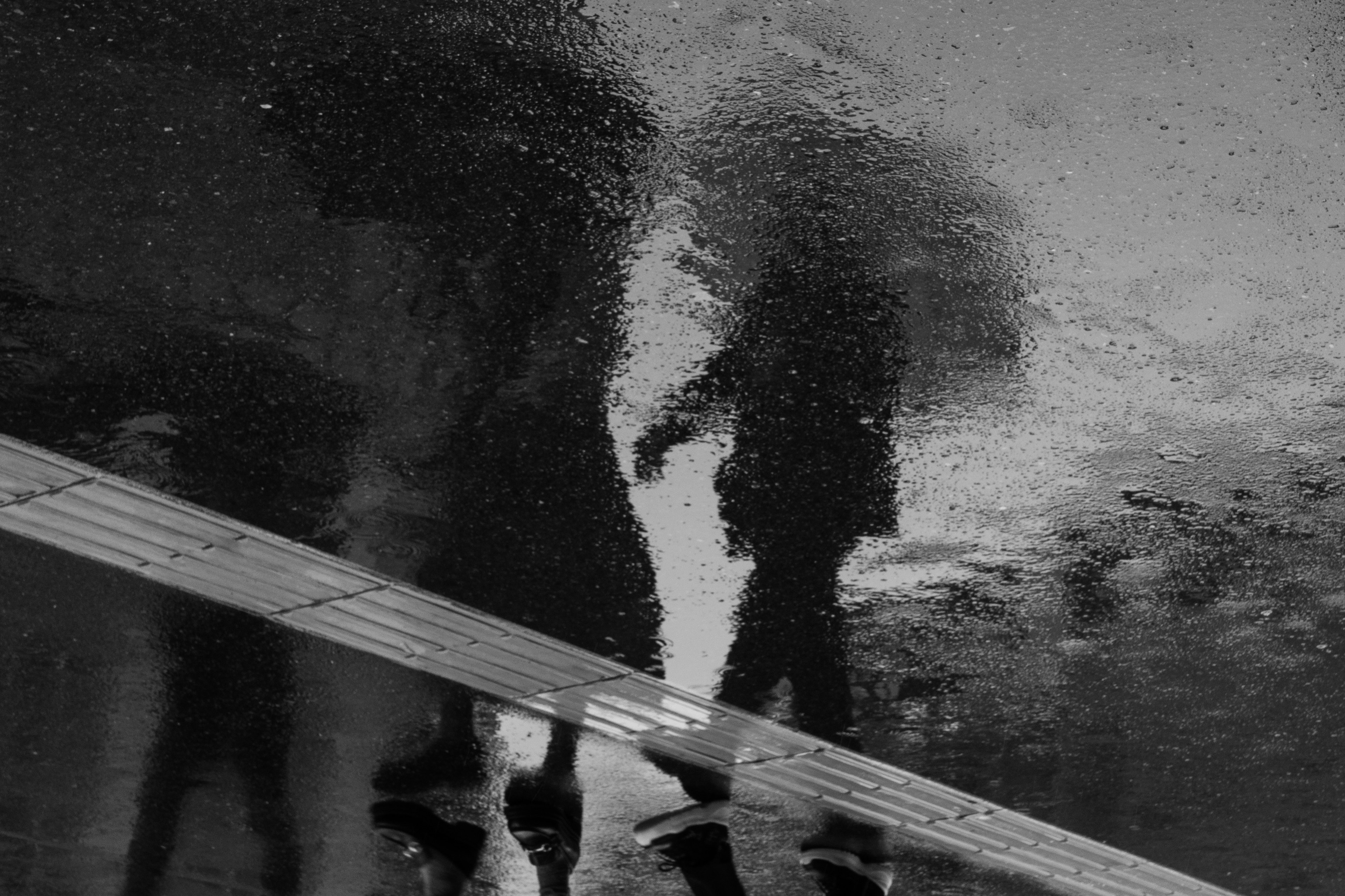 Reflection of two figures holding umbrellas in a puddle during rain